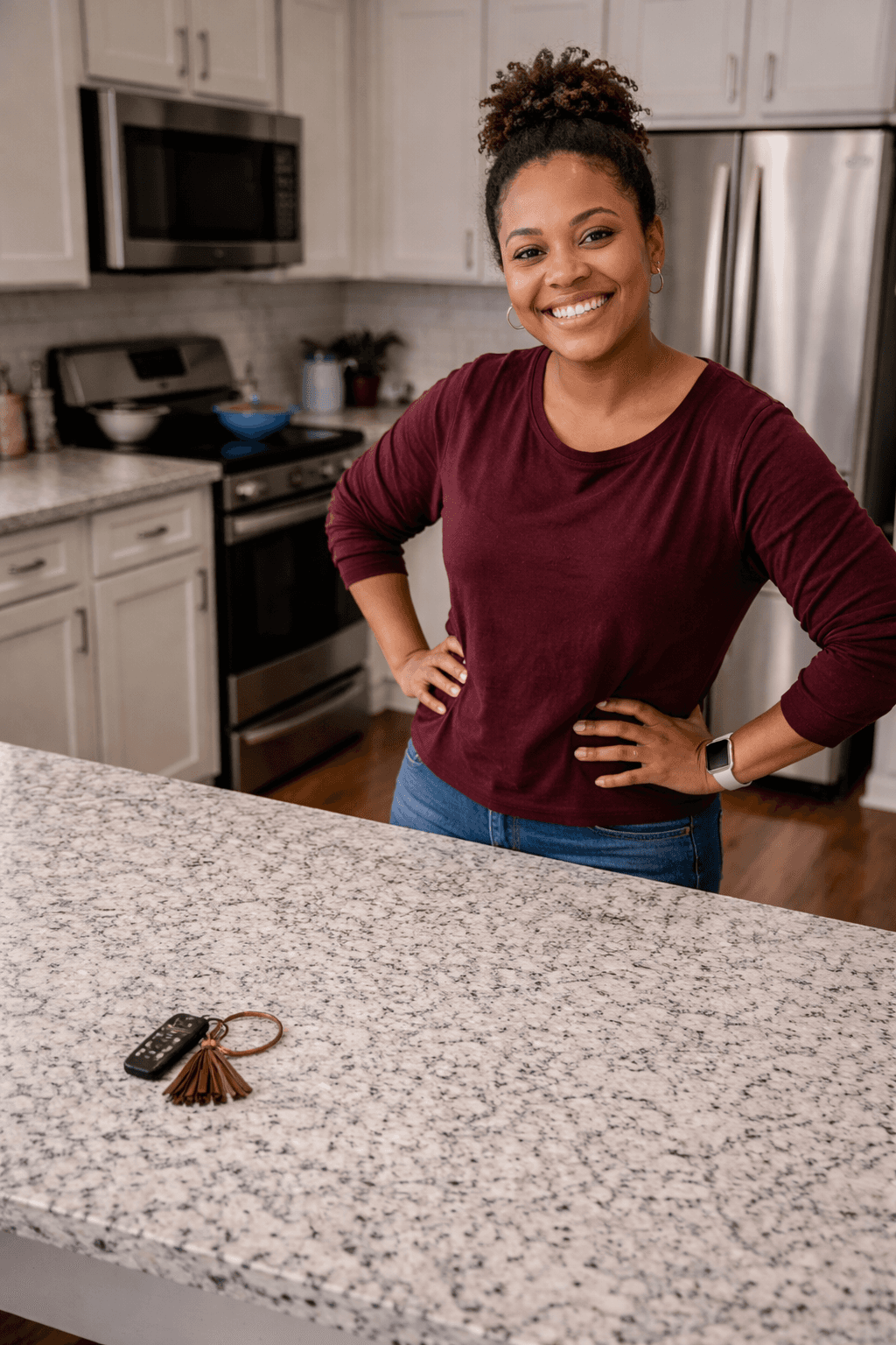 A woman with a bun smiles confidently while standing at a clean and package free granite countertop, hands on her hips.
