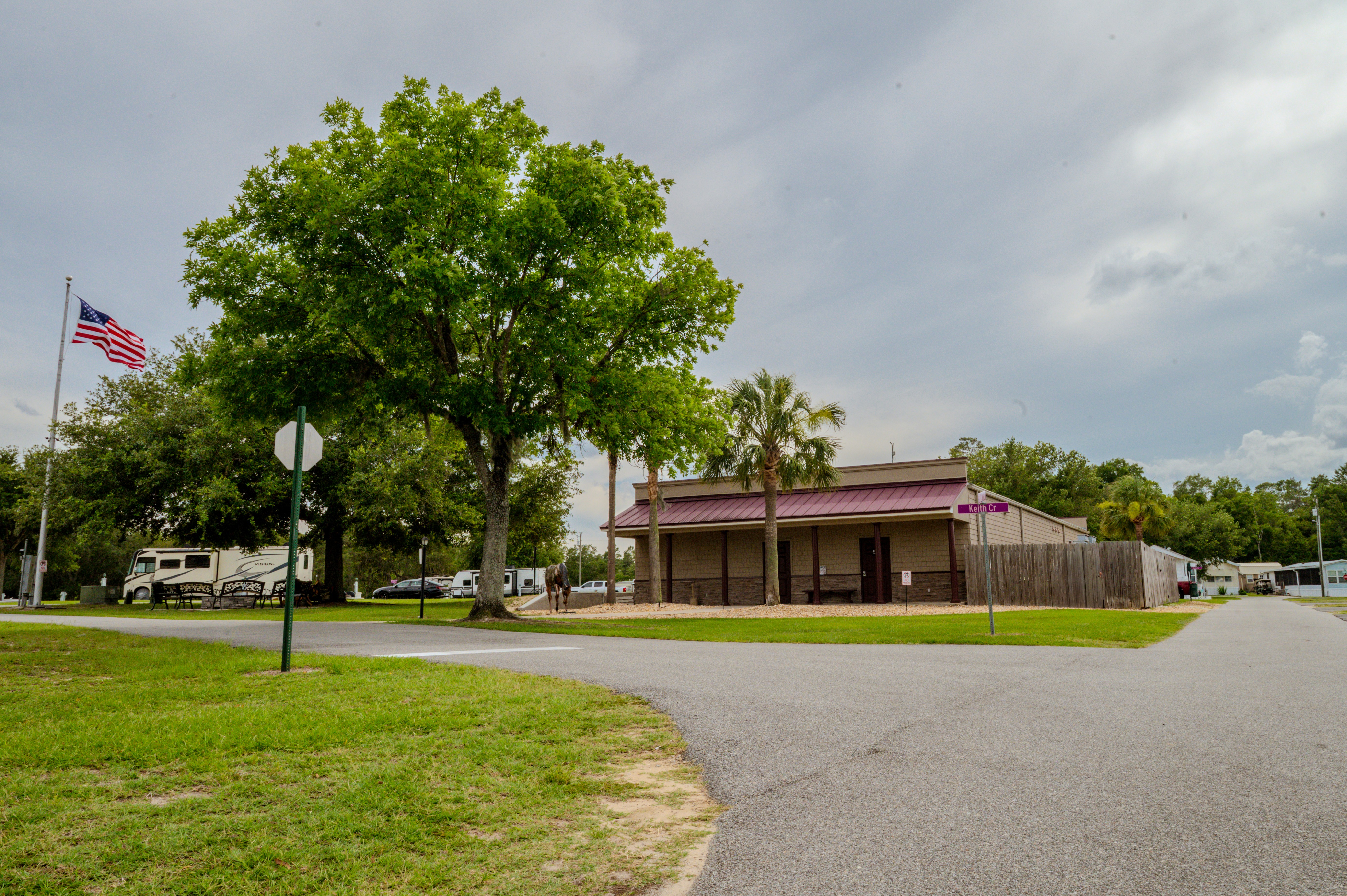 RV resort street with trees, an American flag, benches, and parked RVs