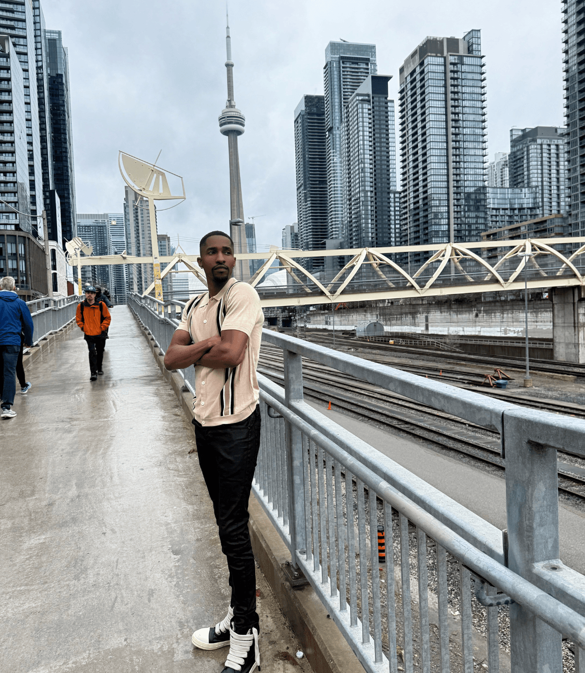 Tyrone “TyFix” Adeyeye stands on a Toronto pedestrian bridge with the CN Tower and skyline behind him.