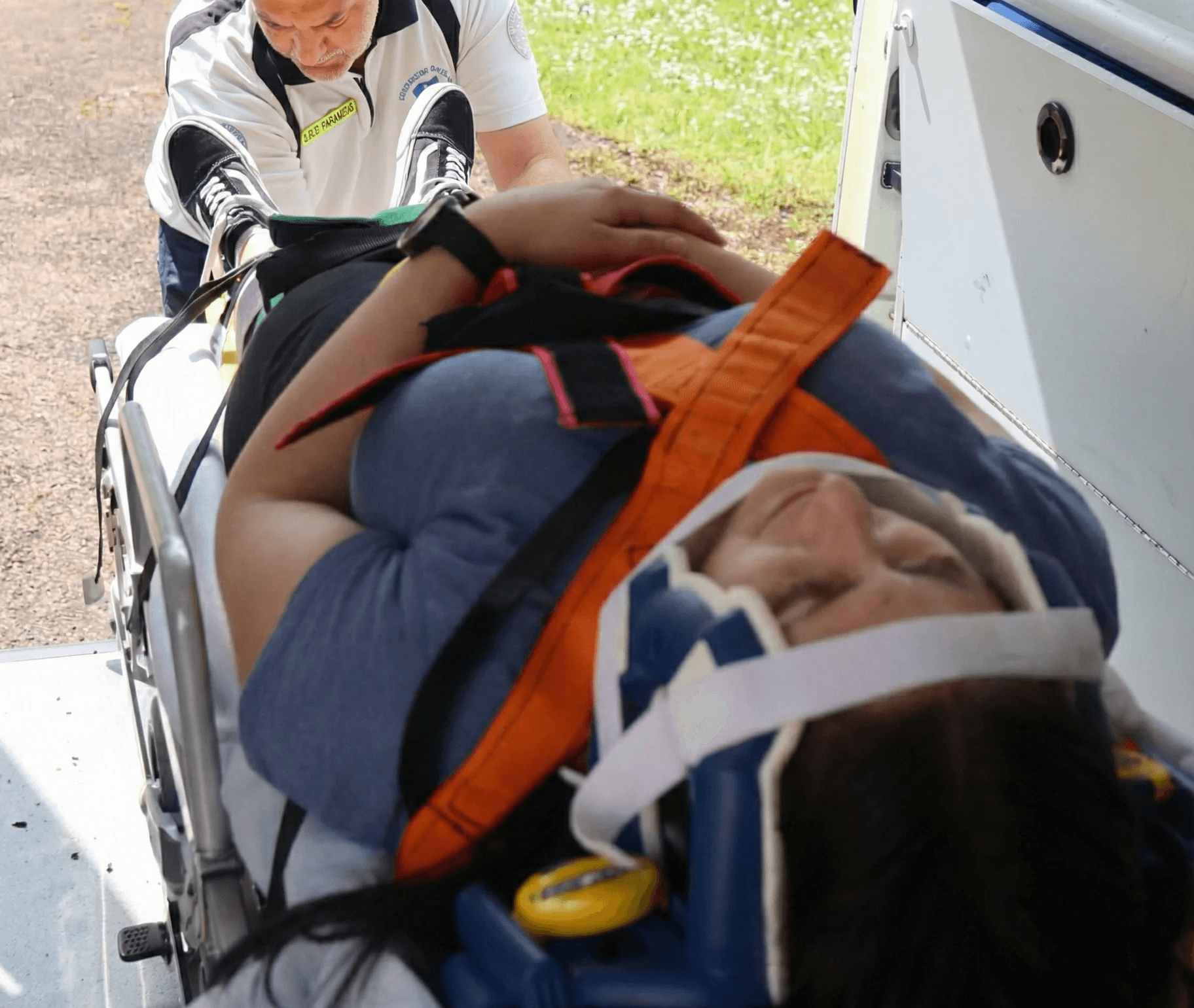 Femme en civière avec col cervical, secouriste la chargeant dans une ambulance.