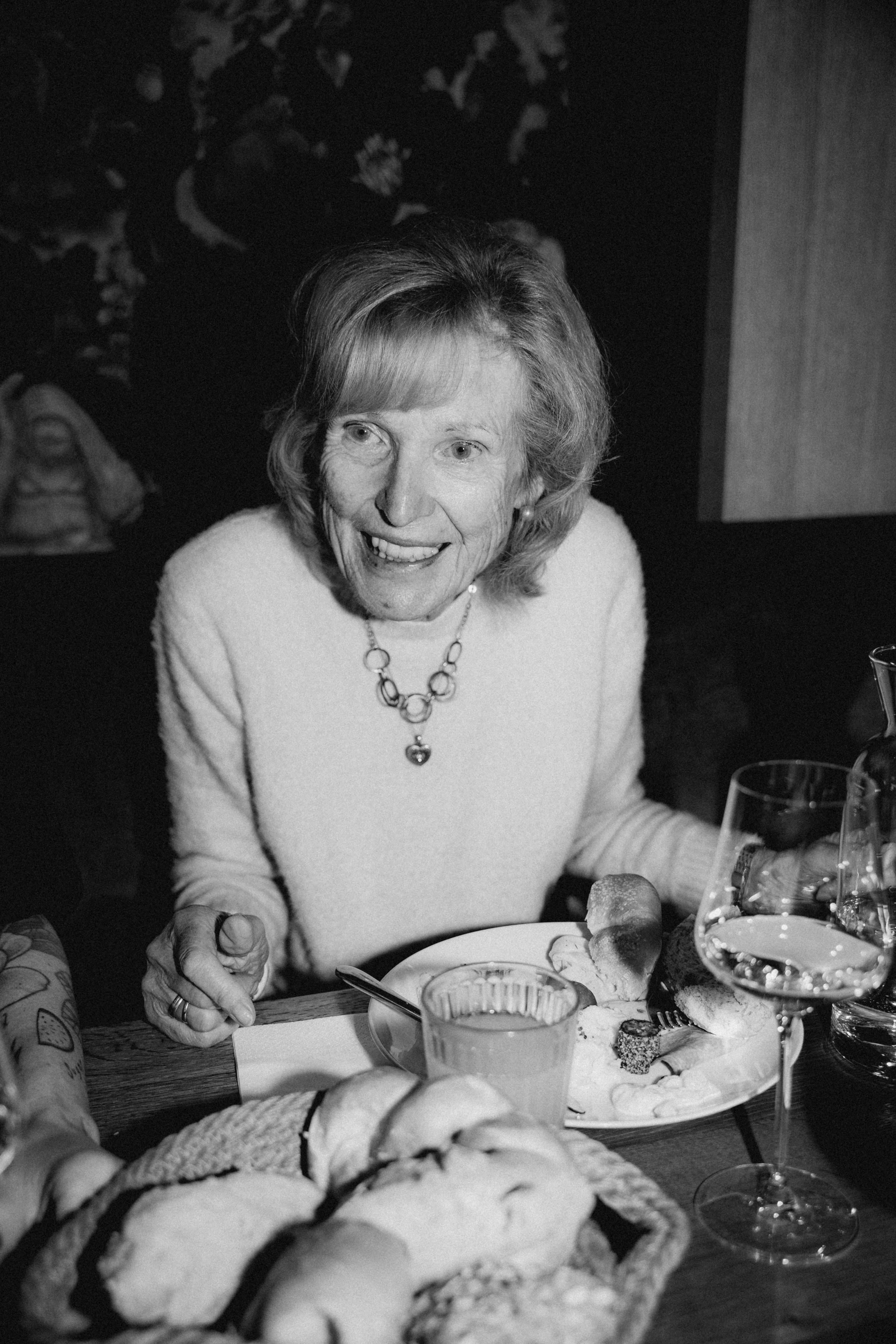 Black and white photograph of an older woman sitting at a table with rolls and drinks, with the caption 'ERNI <3'