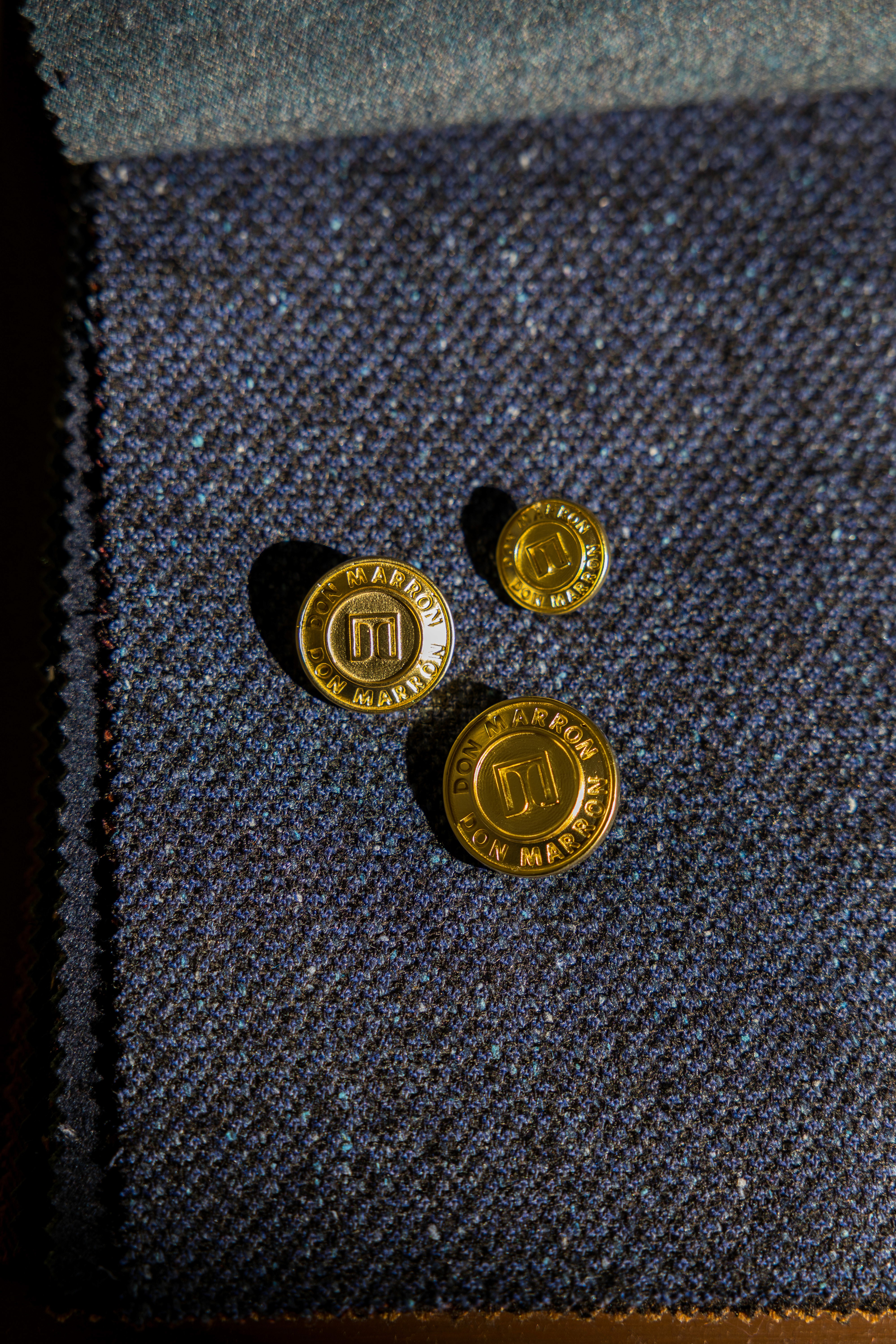 Close-up of a button engraved with the initials DM on a dark tailored jacket, highlighting craftsmanship, fine detailing, and luxury menswear aesthetics.