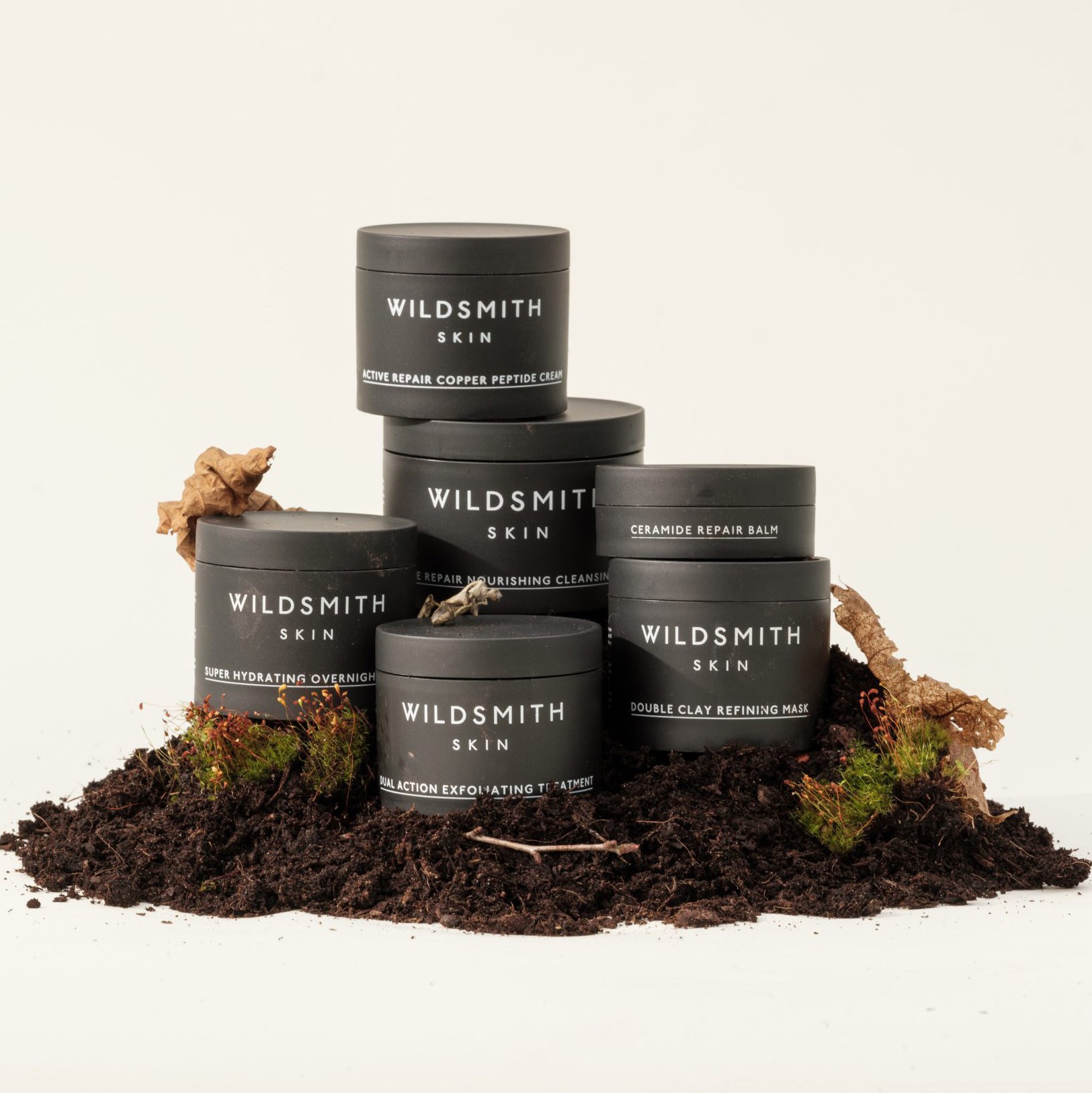 A collection of Wildsmith treatments and moisturisers packaged in various black VIVOMER tubs. The sleek dark finish demonstrates how sustainable petroleum-free materials can meet high-end beauty aesthetics.