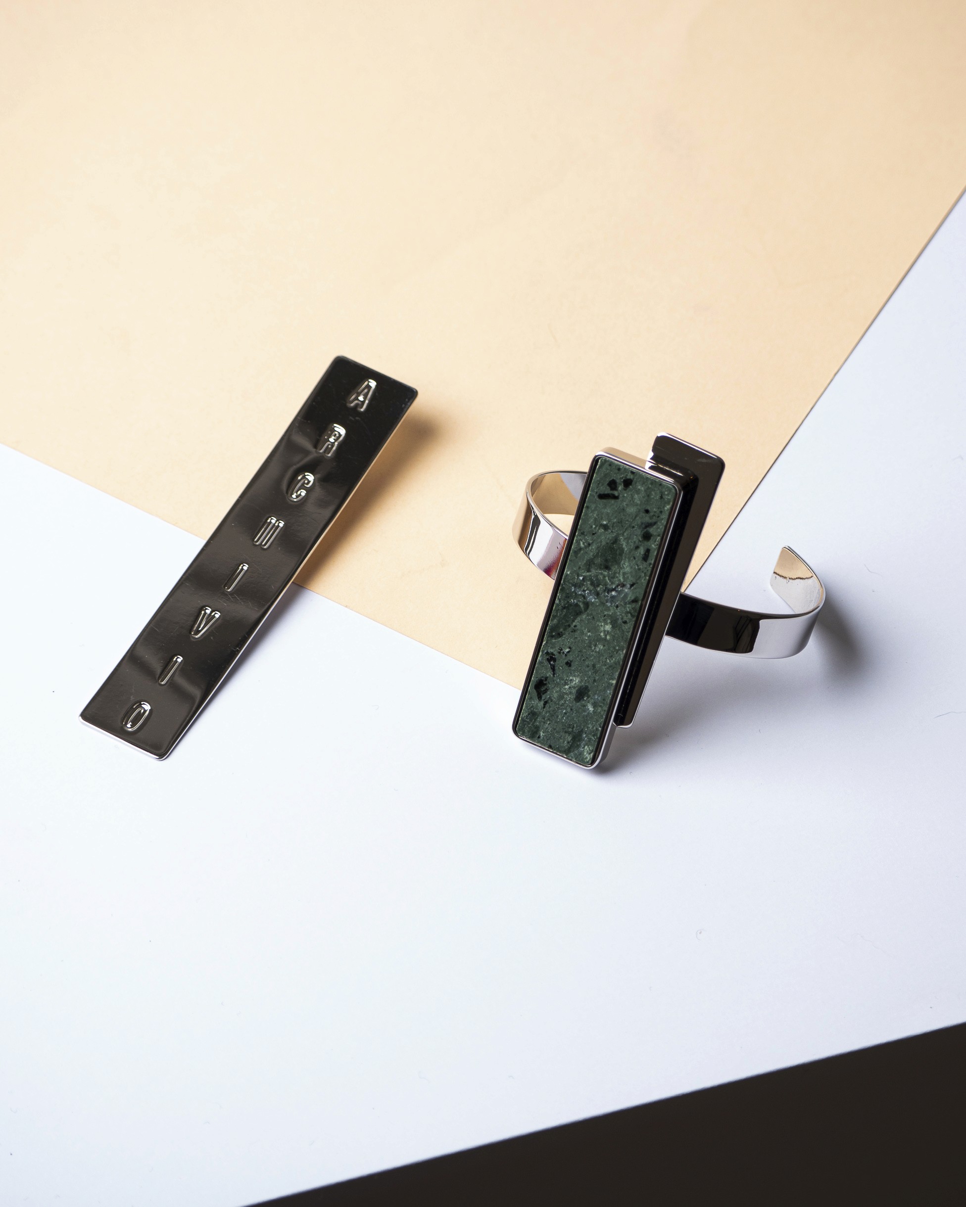 Photo studio d'un bracelet avec une pièce de marbre vert rectangulaire montée et d'une boucle d'oreille rectangulaire et allongée de la marque Archivio sur des feuilles colorées blanches et beige