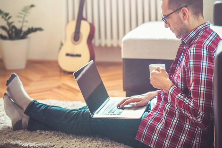 Man sitting on floor with laptop and coffee cup at home
