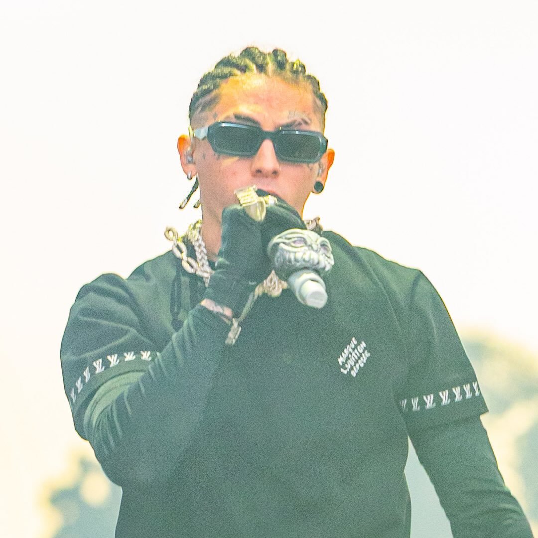 Foto de perfil de KHEA en blanco y negro, con trenzas y manos en la cabeza, mirando fijamente a la cámara.