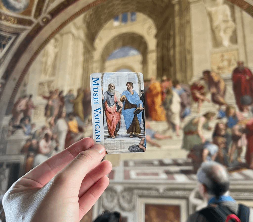Visitor holding a Musei Vaticani ticket in front of Raphael’s School of Athens inside the Vatican Museums.