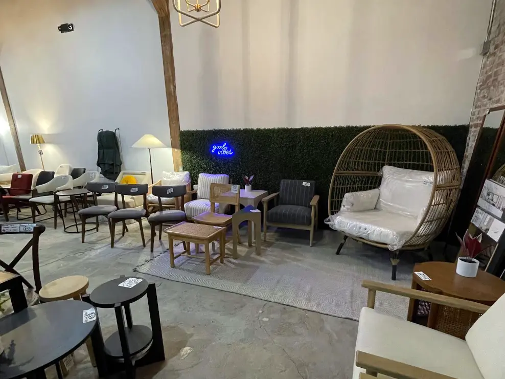 Stylized furniture showroom featuring accent chairs, wood tables, lighting, and a wicker lounge chair display