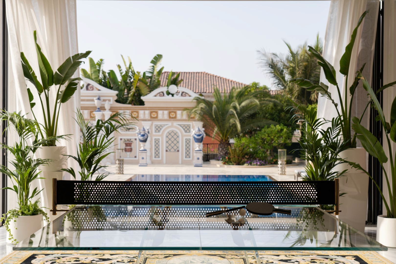 Elegant patio view with lush tropical plants, ornate columns, and a clear blue swimming pool under a bright sky.