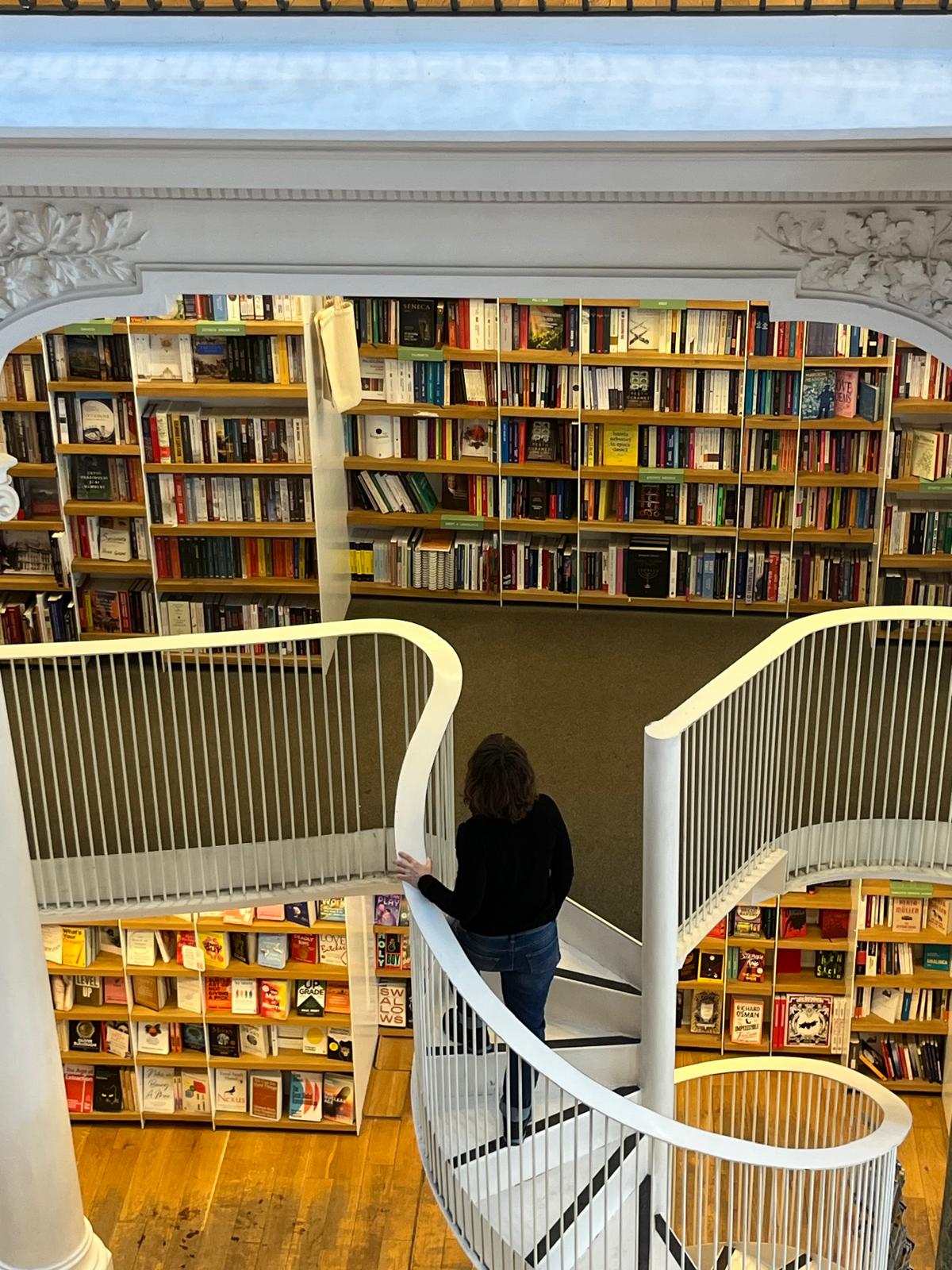 A person browsing books beside a curved staircase in a multi-level library.
