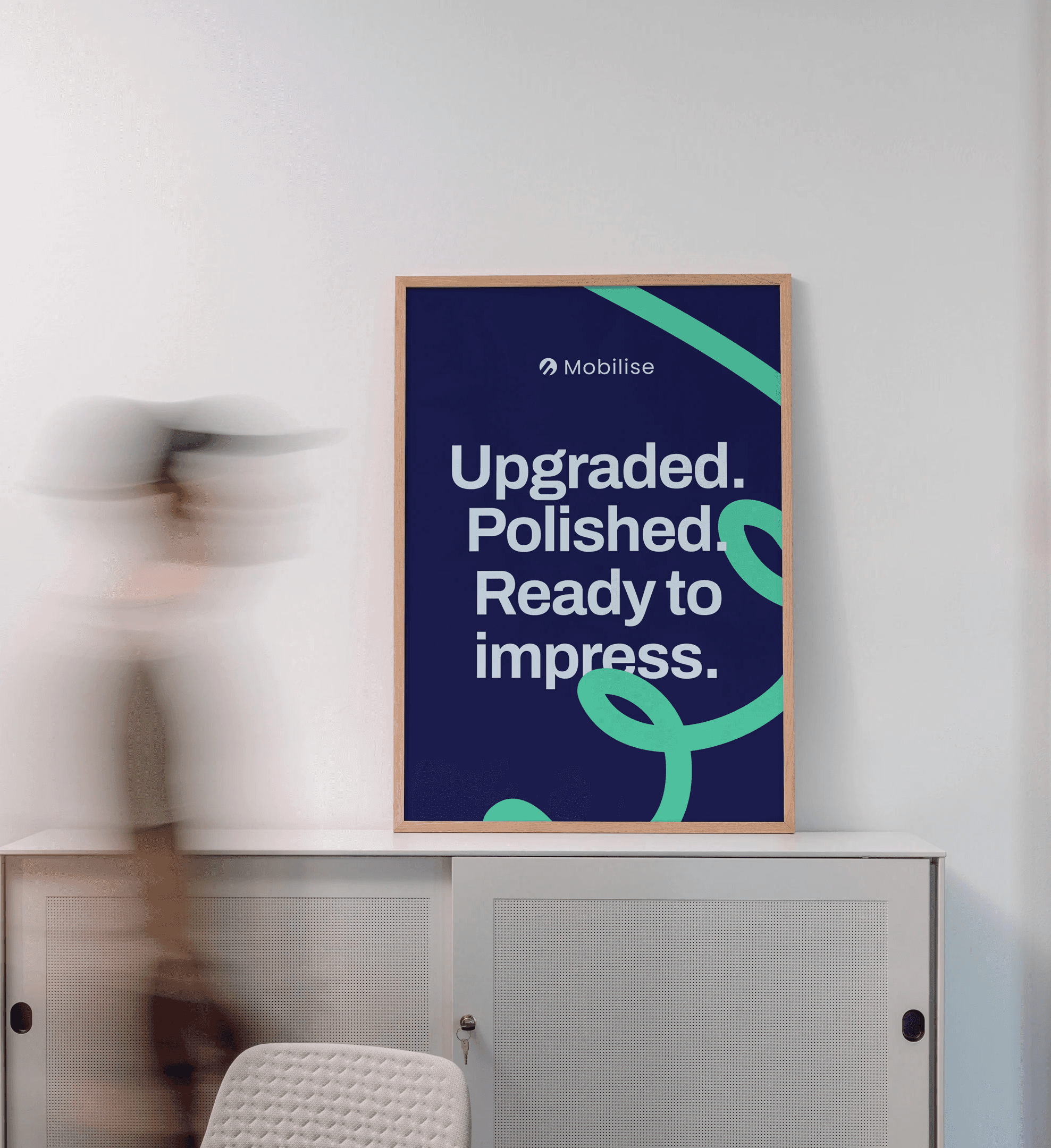 Framed Mobilise brand poster on a wall with a blurred person walking past.