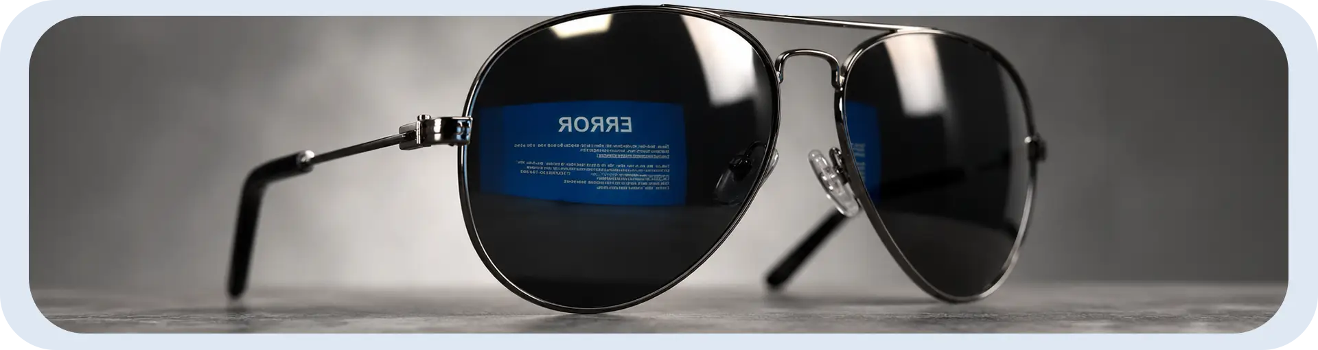 Fotografia em close de óculos de sol estilo aviador sobre uma superfície cinza escuro. O detalhe principal é o reflexo na lente esquerda, que mostra uma tela azul de computador com a palavra 'ERROR' refletida de forma invertida, sugerindo que os óculos estavam de frente para um monitor com falha de sistema.