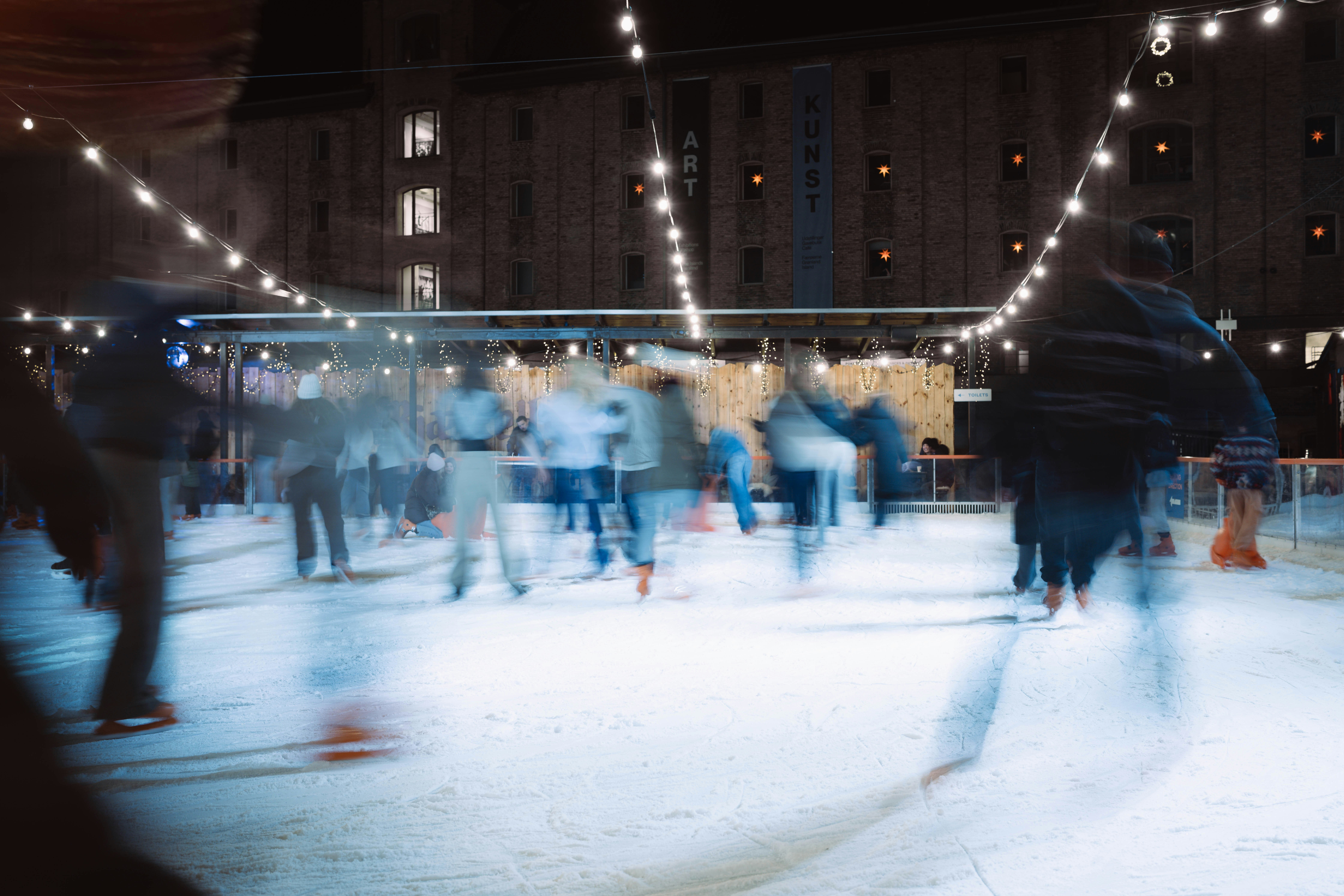 People ice skating at night with string lights.