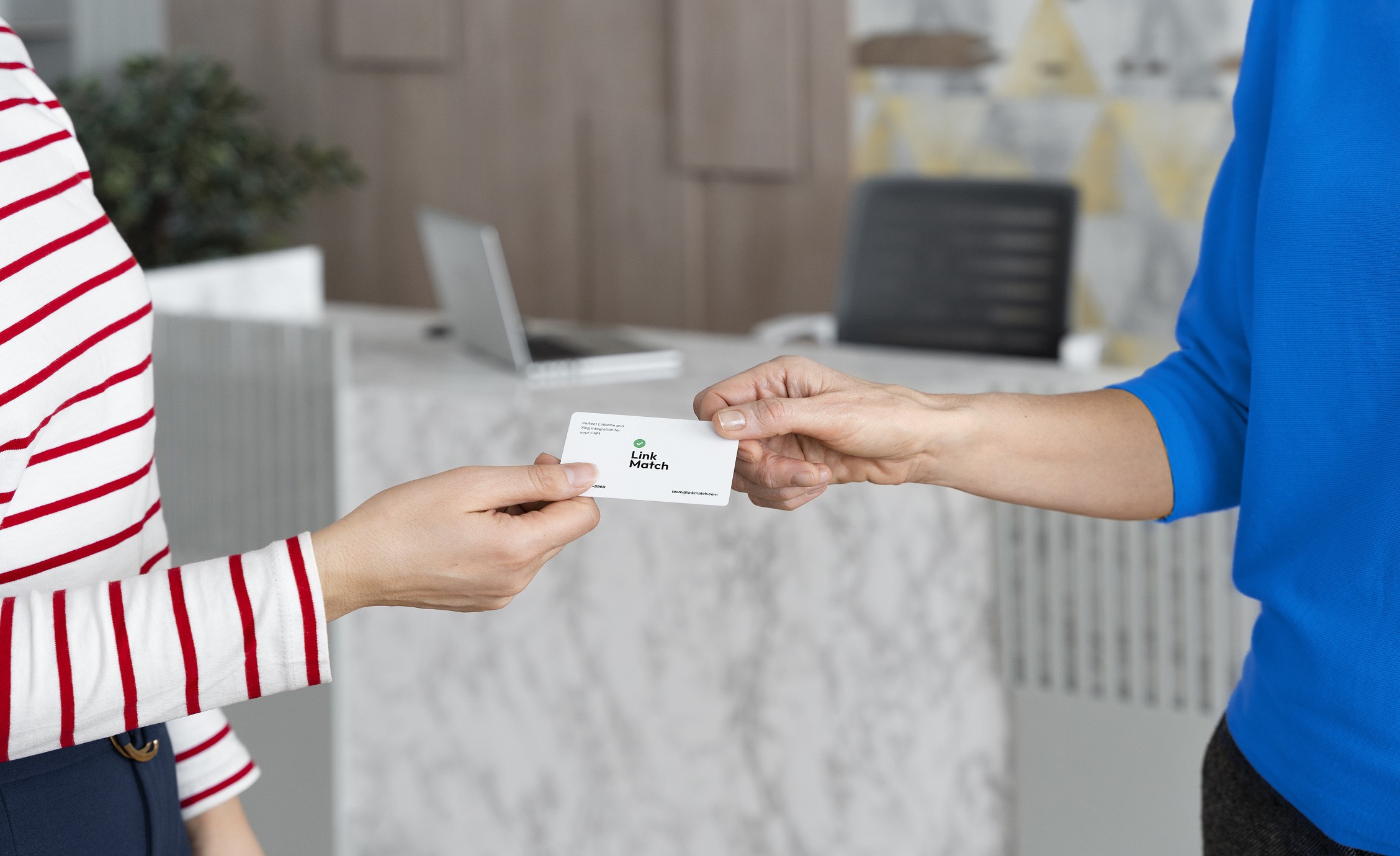 Two individuals exchanging a LinkMatch branded business card in a modern office environment