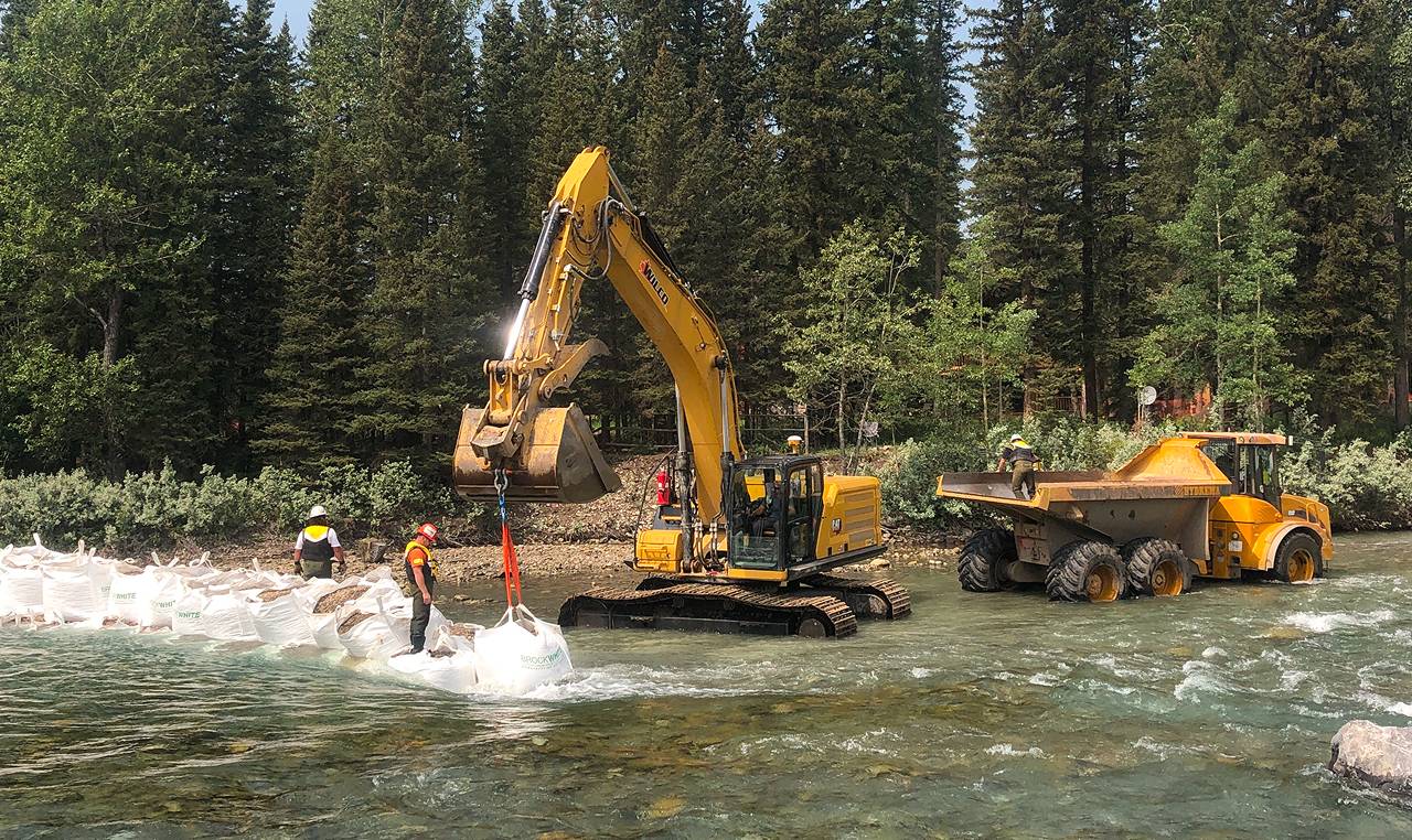 Excavator placing super sacks for temporary river isolation at Bragg Creek flood mitigation site