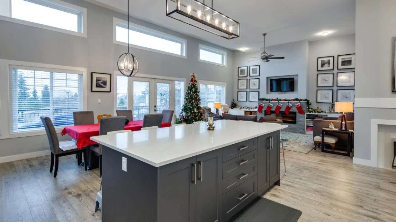 Spacious open-concept kitchen and living area with dramatic vaulted ceilings, large charcoal gray island with white quartz countertops, contemporary linear chandeliers, and floor-to-ceiling windows in custom Burnaby home
