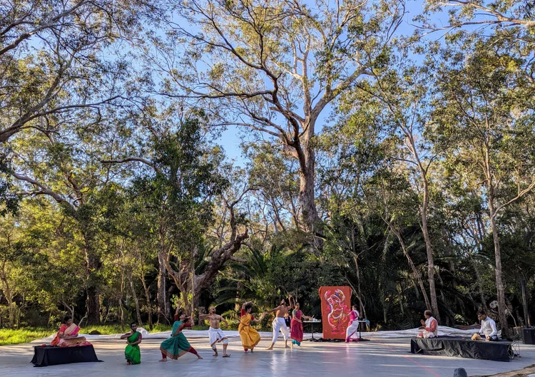 A person with shoulder-length blonde hair wearing a black newsboy cap and a black sweater.