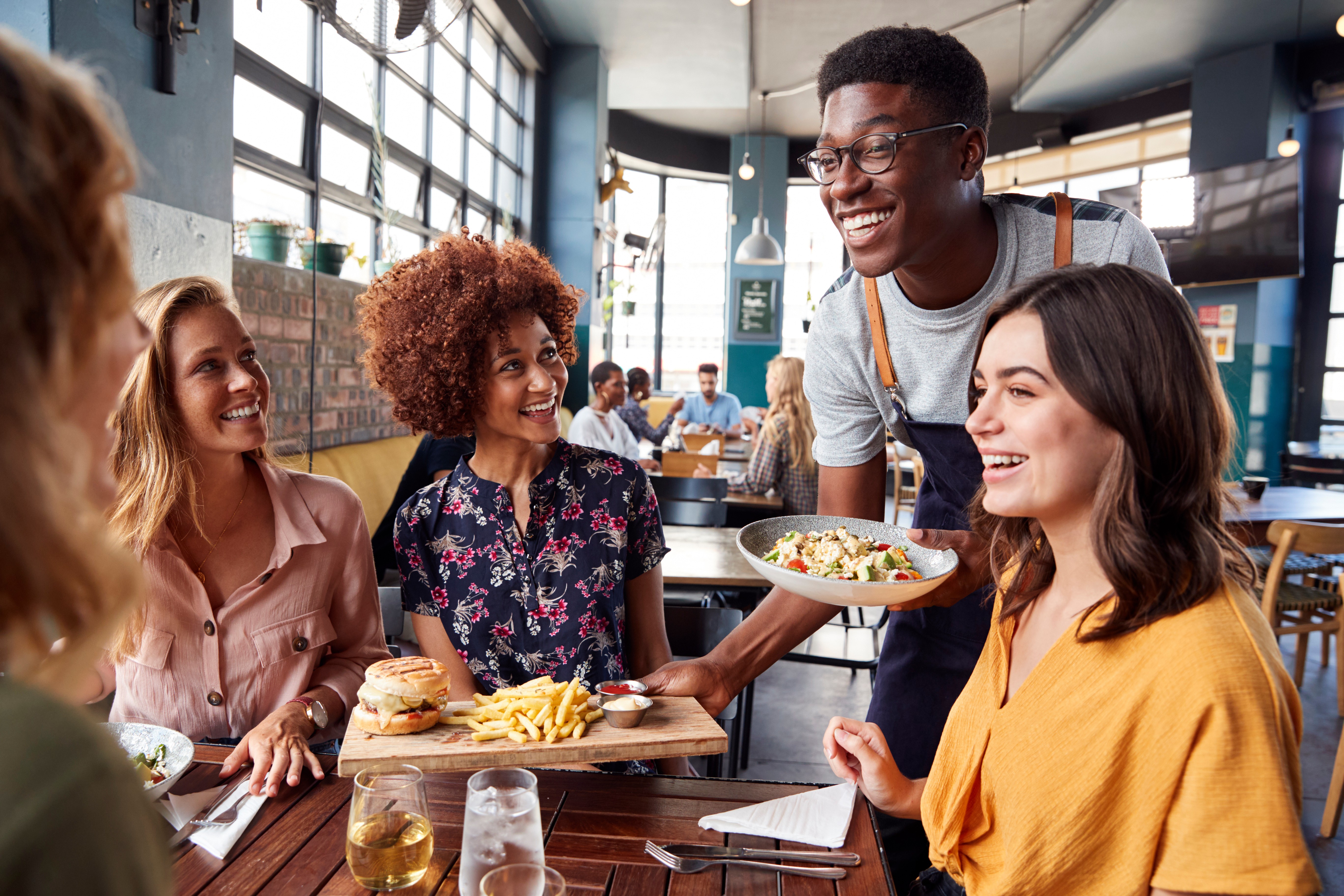 Waiter smiling whilst serving a group of friends at a restaurant.