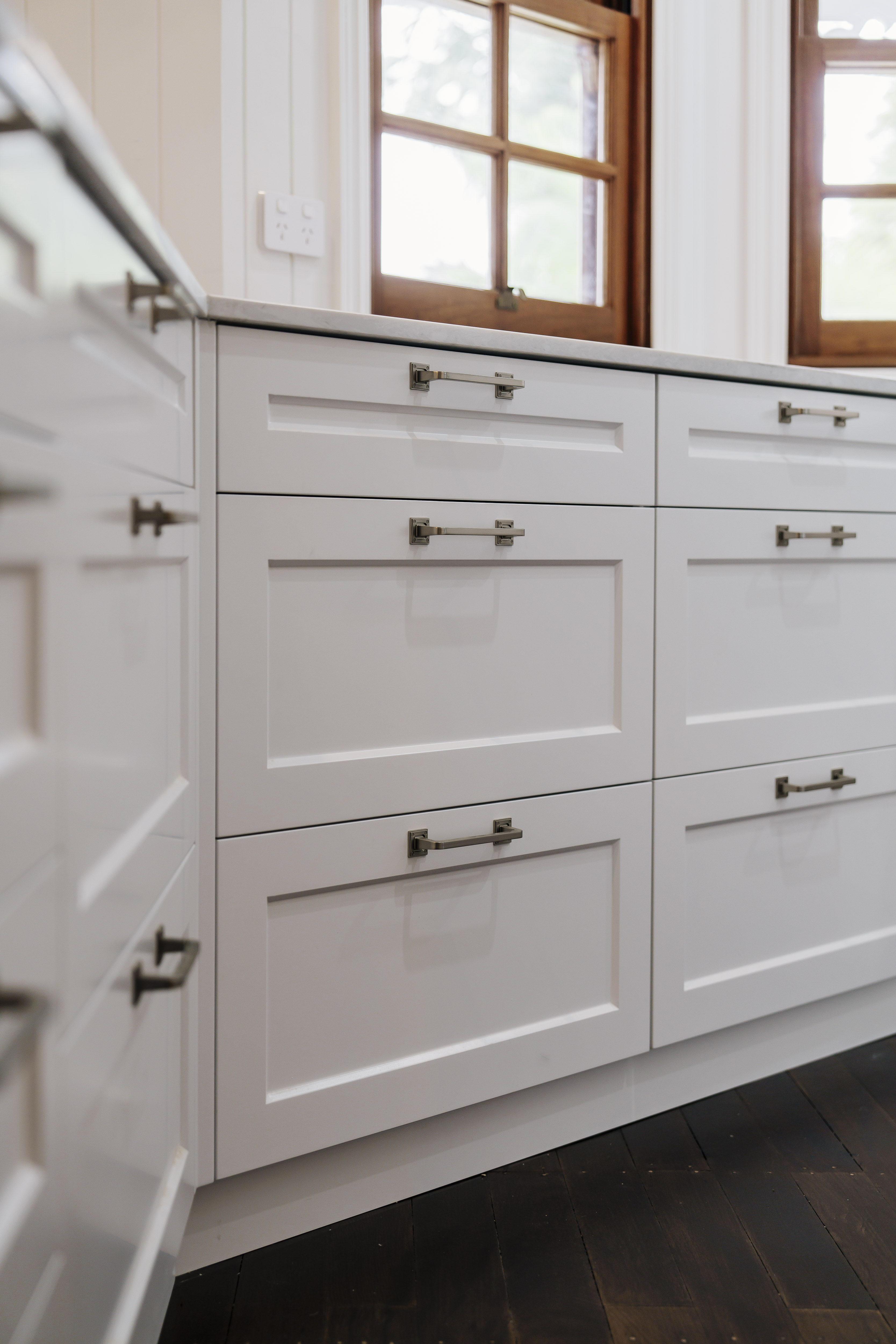 White shaker kitchen drawers with nickel handles under original timber windows in a heritage house