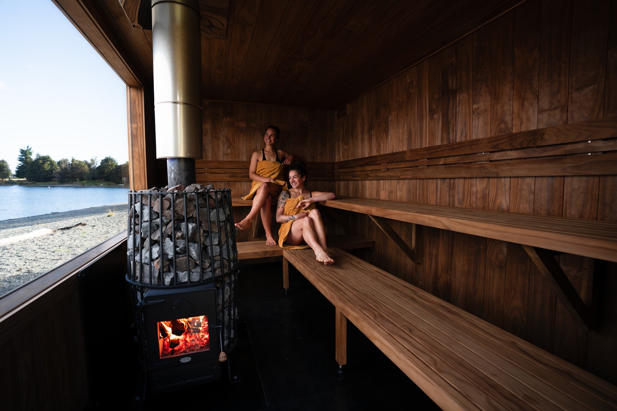 A group of five people relax and chat in a cozy, wooden sauna. They sit on benches with towels, surrounded by warm tones, creating a peaceful atmosphere.