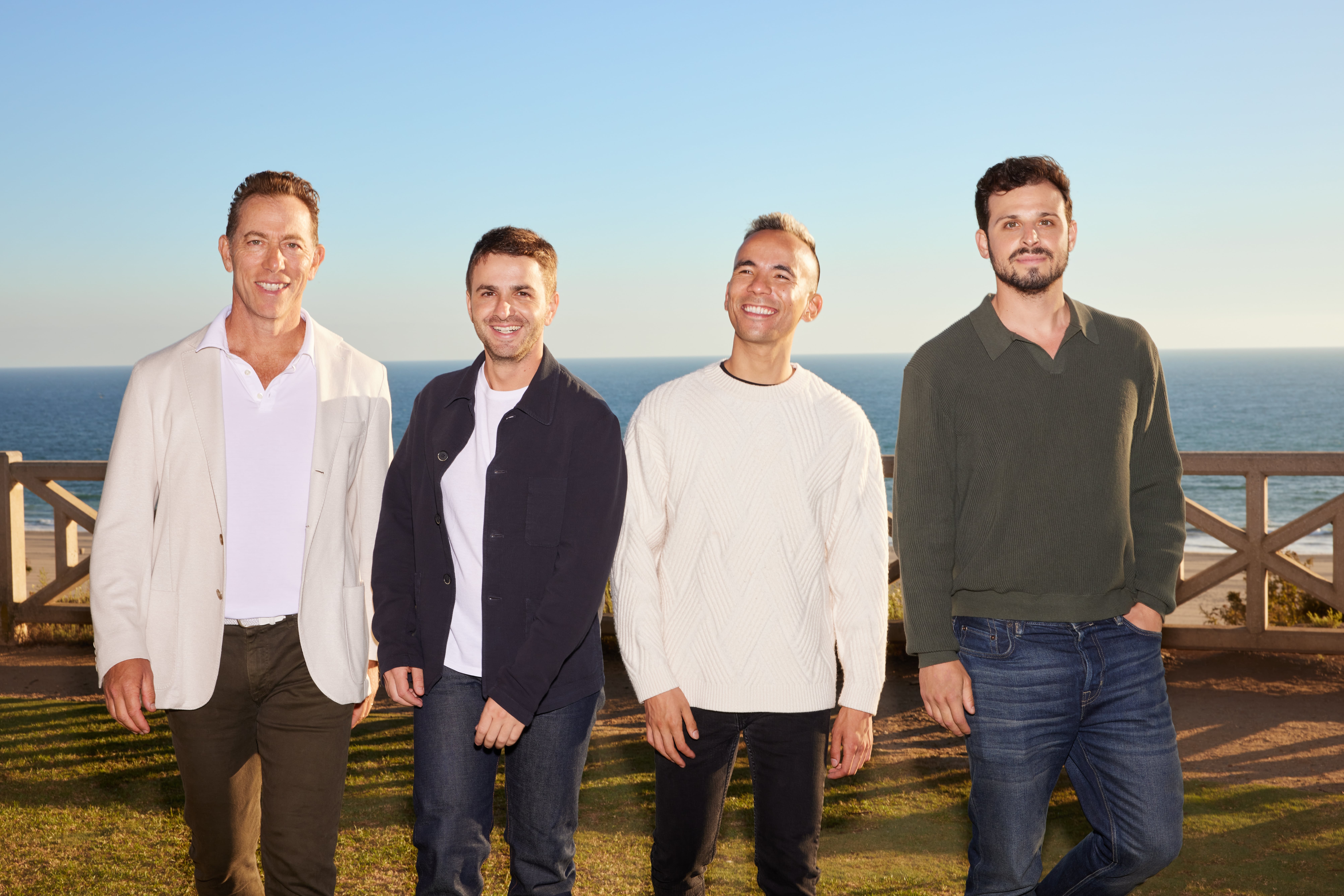 Kenny Stevens Team stand together outdoors, smiling, with a scenic background of a coastline and clear sky.
