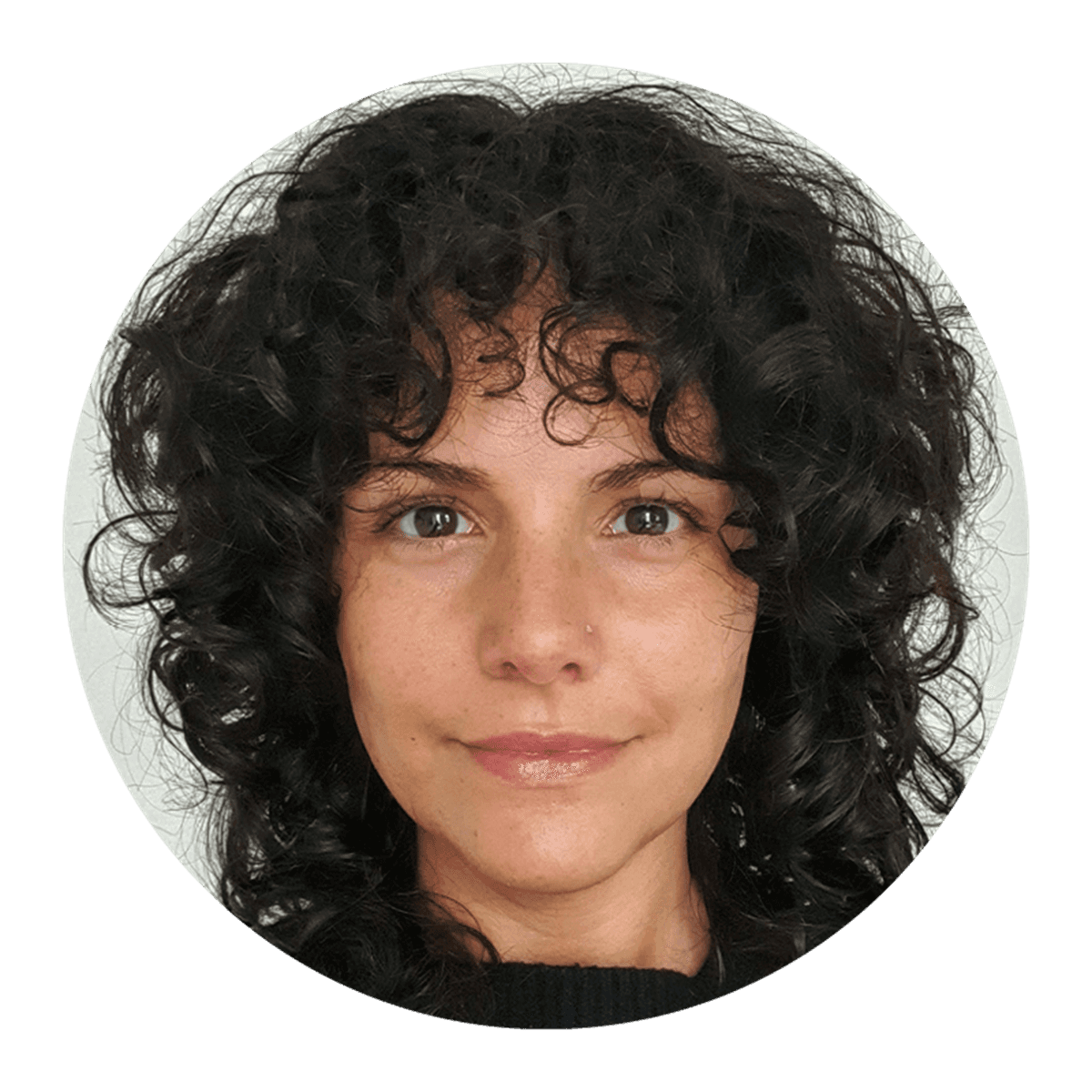 A circular head‑and‑shoulders portrait of a person with dark, curly hair against a plain light background, wearing a dark top