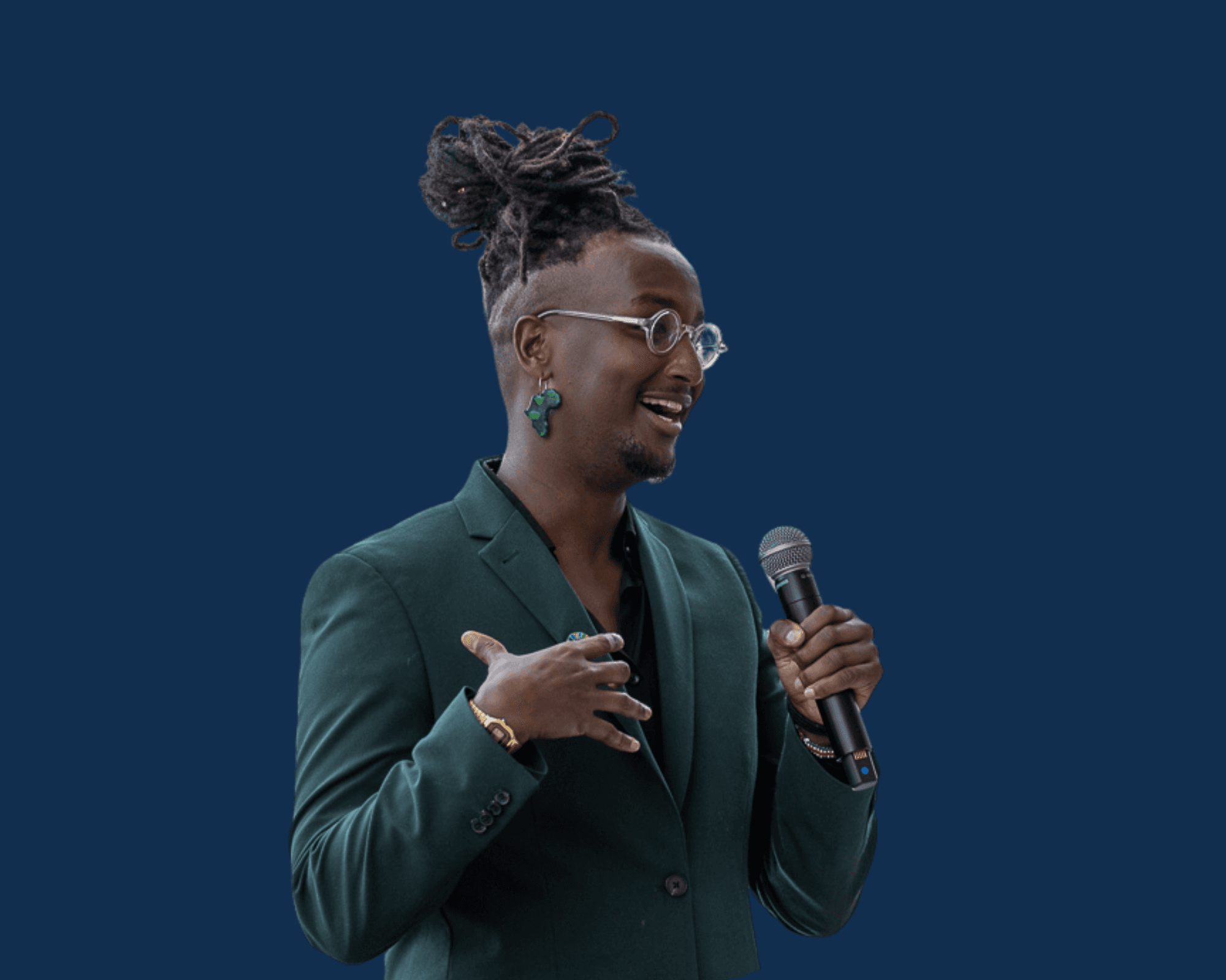 A person with glasses and a bun hairstyle gestures while speaking, wearing a dark green blazer against a blue background.