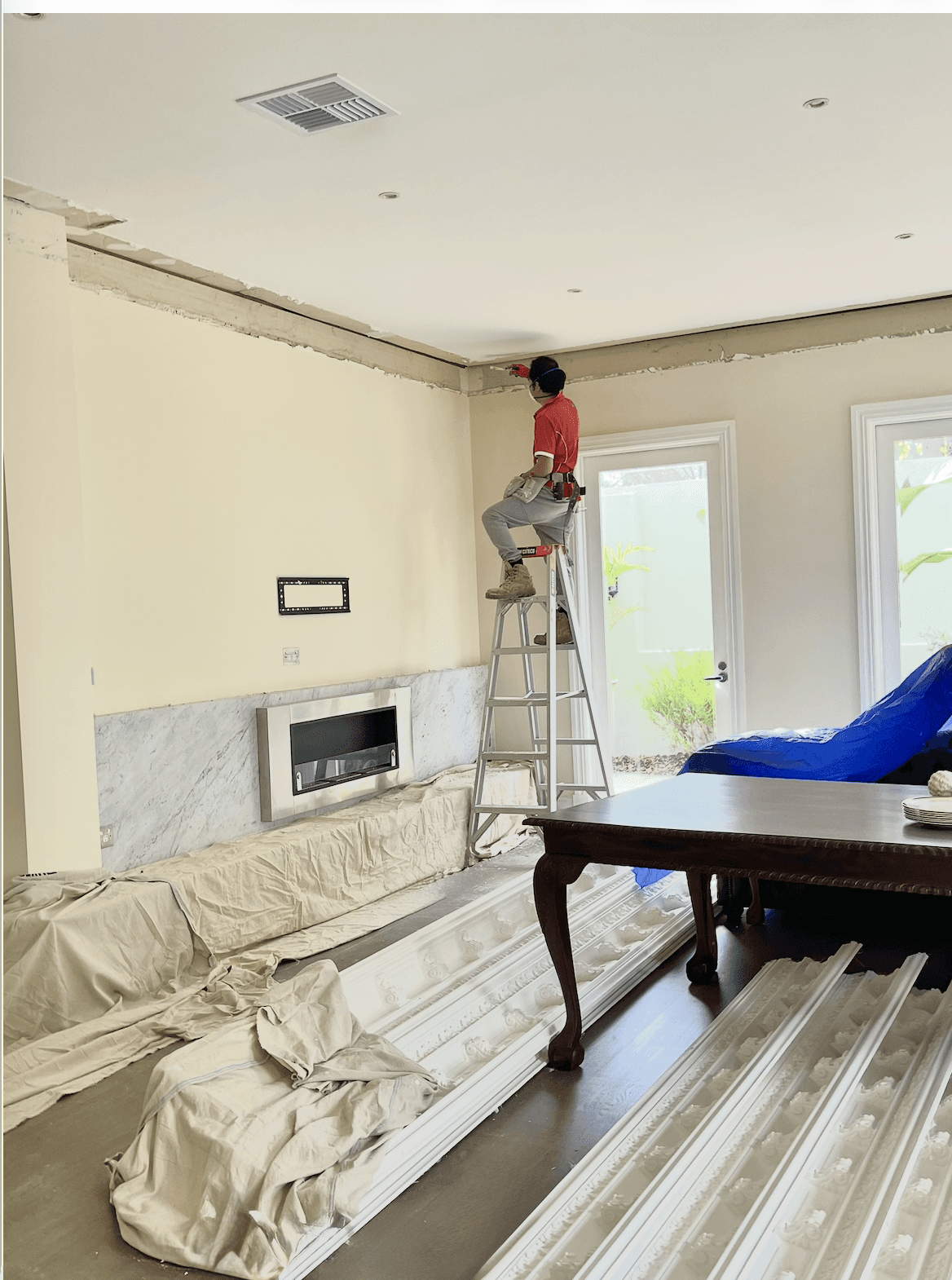 Modern living room with abstract art, beige sectional sofa, indoor plants, and large windows.