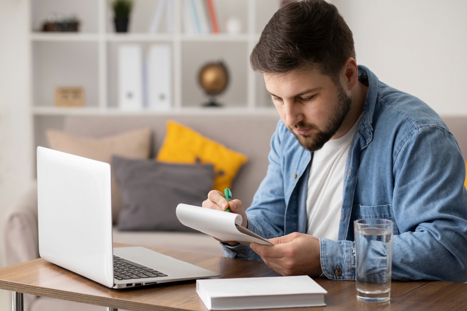 A man sits at a table, focused on his laptop, with a notebook open beside him, engaged in work or study.