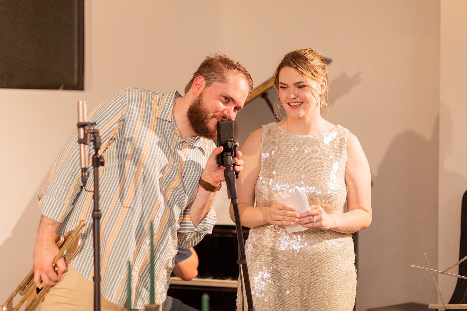 Alex leaning over to speak into a microphone with his wife Tess looking towards him smiling