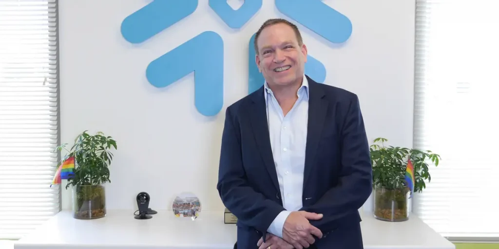 Man in a suit standing in front of the Snowflake logo in an office
