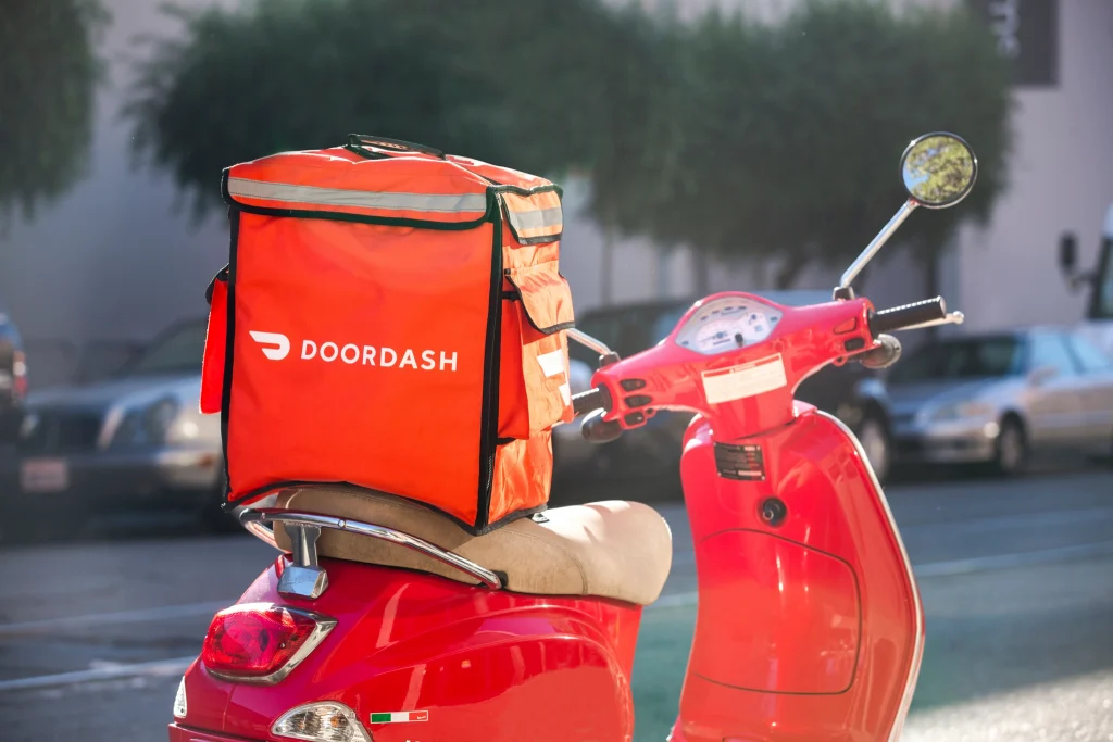Red scooter with an orange DoorDash delivery bag, illustrating restaurant food delivery