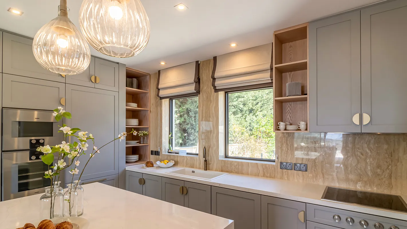 White Cedar House Mediterranean kitchen with grey cabinetry, marble-look backsplash, and pendant lighting