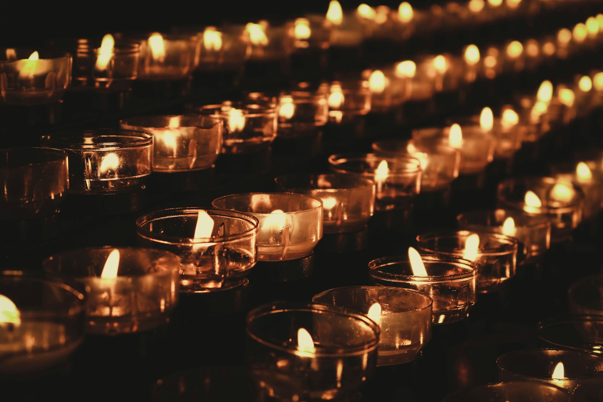 Rows of lit votive candles in a dark chapel
