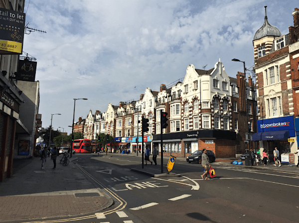 A smiling man with curly hair is sitting at a desk, looking at the camera, with a laptop and a lamp in the background.