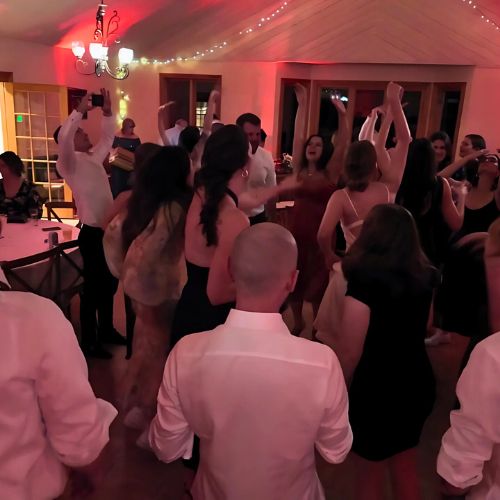 A newlywed couple dancing together under the soft, colorful lighting of the wedding banquet room, with guests clapping and smiling around them.