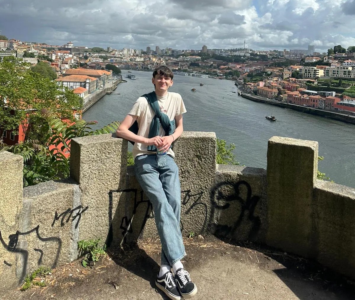 Daniel leaning against a wall with a background of a river.