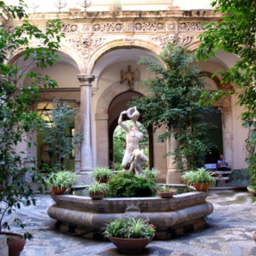 中央に彫刻された噴水がある中庭は、緑に囲まれ、柱やアーチ型の壁に華やかなデザインが施されています。