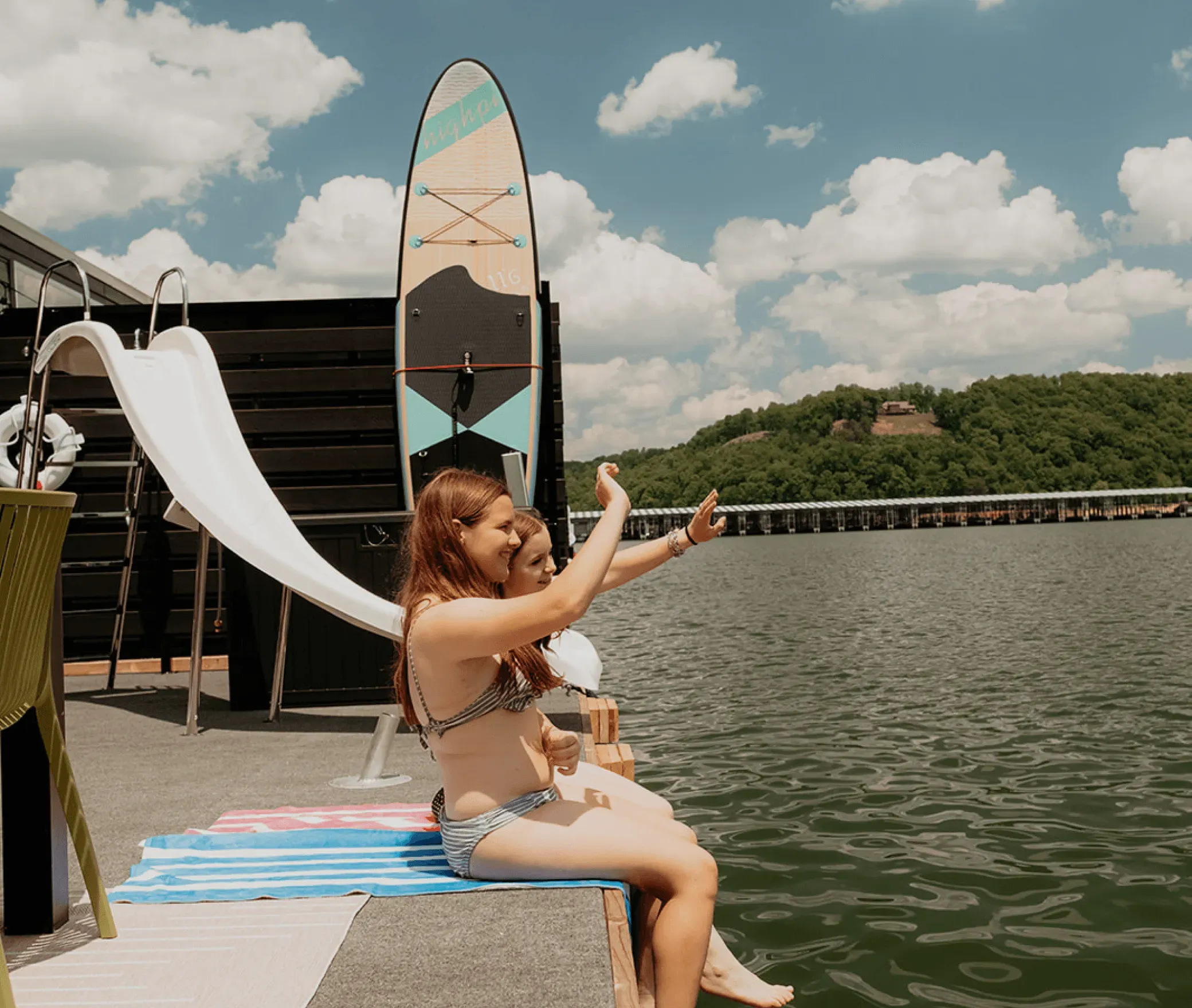 two girls waving to friends by the waterslide that comes standard on both floathomes