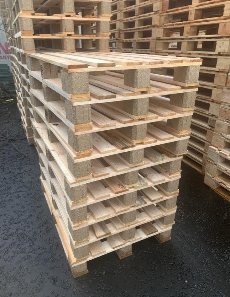Stack of neatly arranged wooden pallets on an asphalt surface, with more stacks in the background.