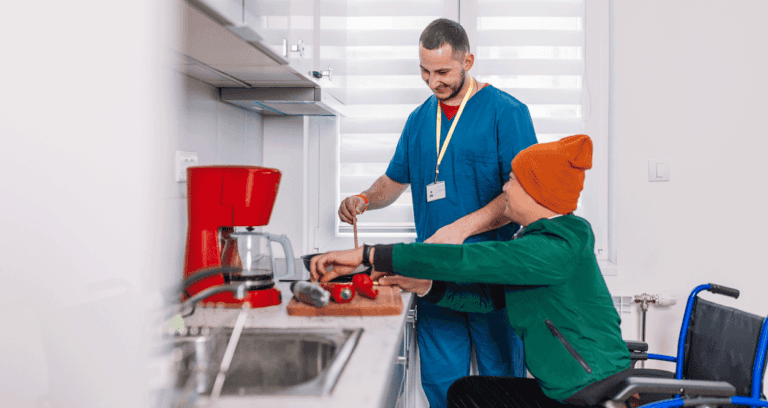 Caregiver assisting a person in a wheelchair with food preparation in a kitchen.