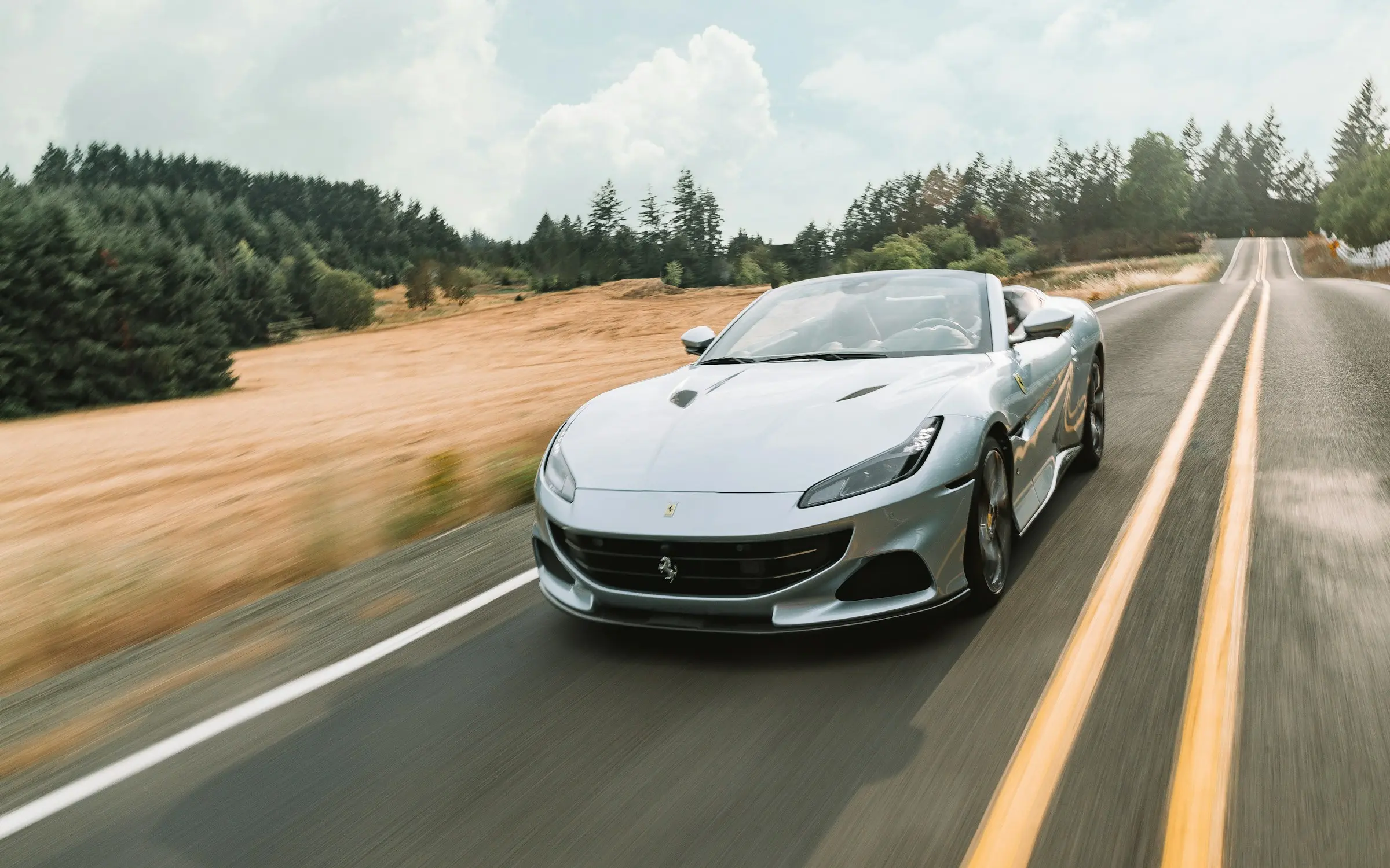 Silver convertible sports car driving on an open highway through a rural landscape during daylight