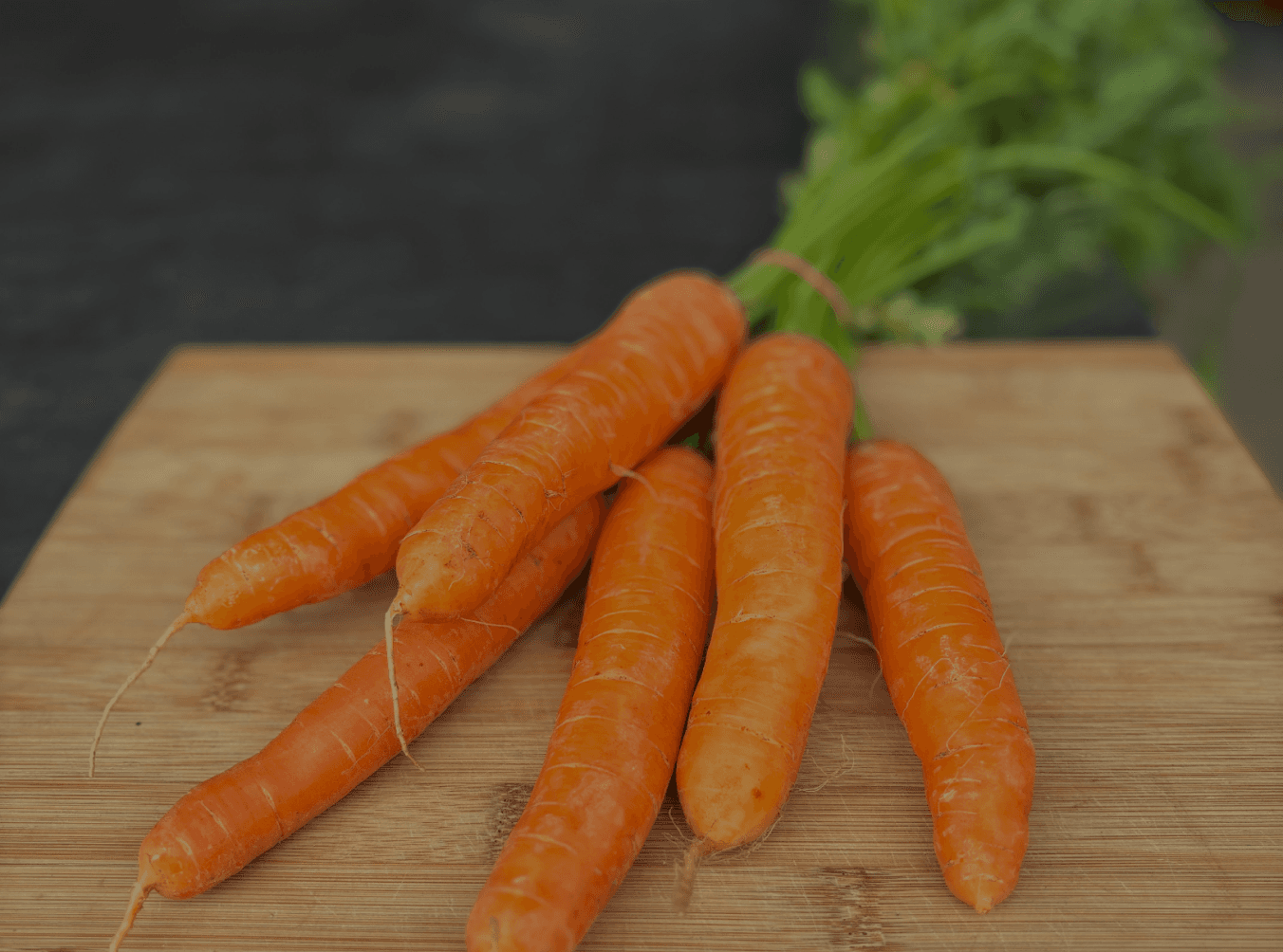 Fresh orange carrots resting on a wooden cutting board.