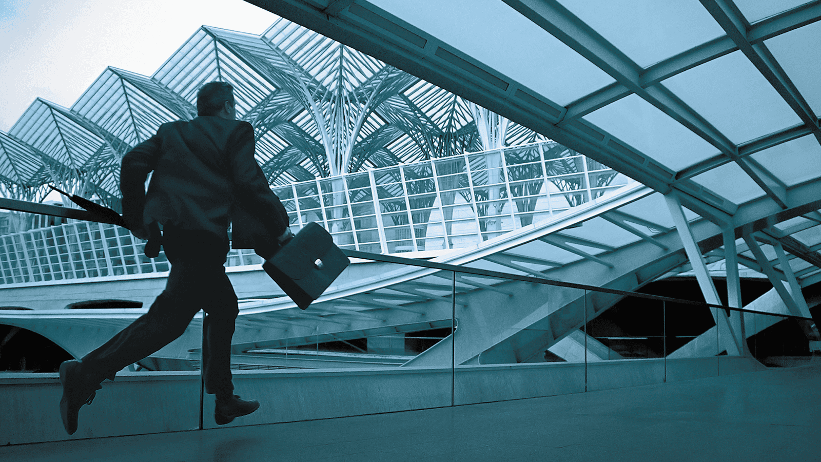 A person in a suit runs with a briefcase through a modern, glass-covered architectural structure.