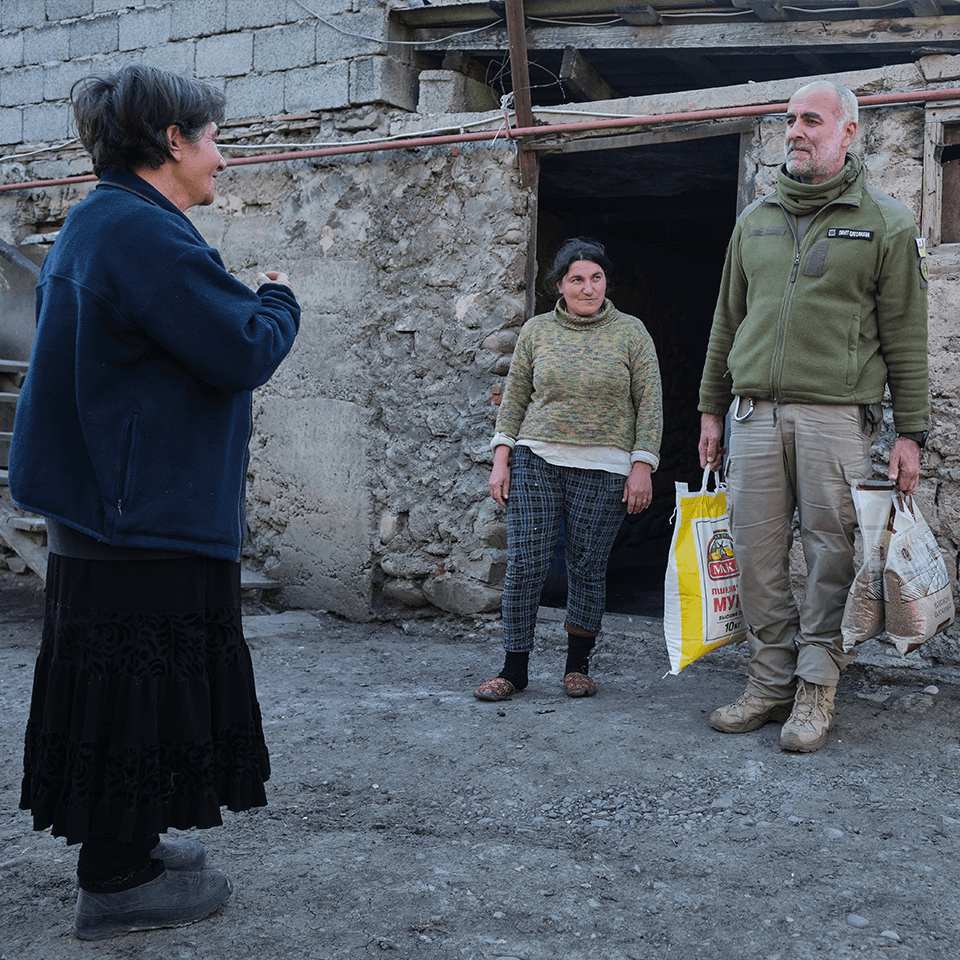 A volunteer handing bags of humanitarian aid to residents in a yard