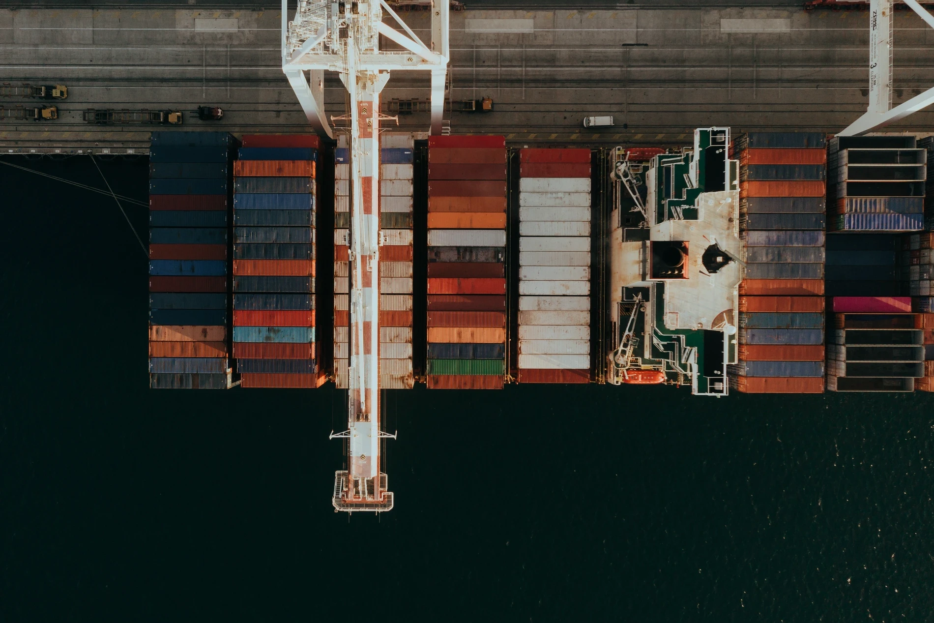 Aerial looking straight down on a container ship being loaded, a crane spanning its deck
