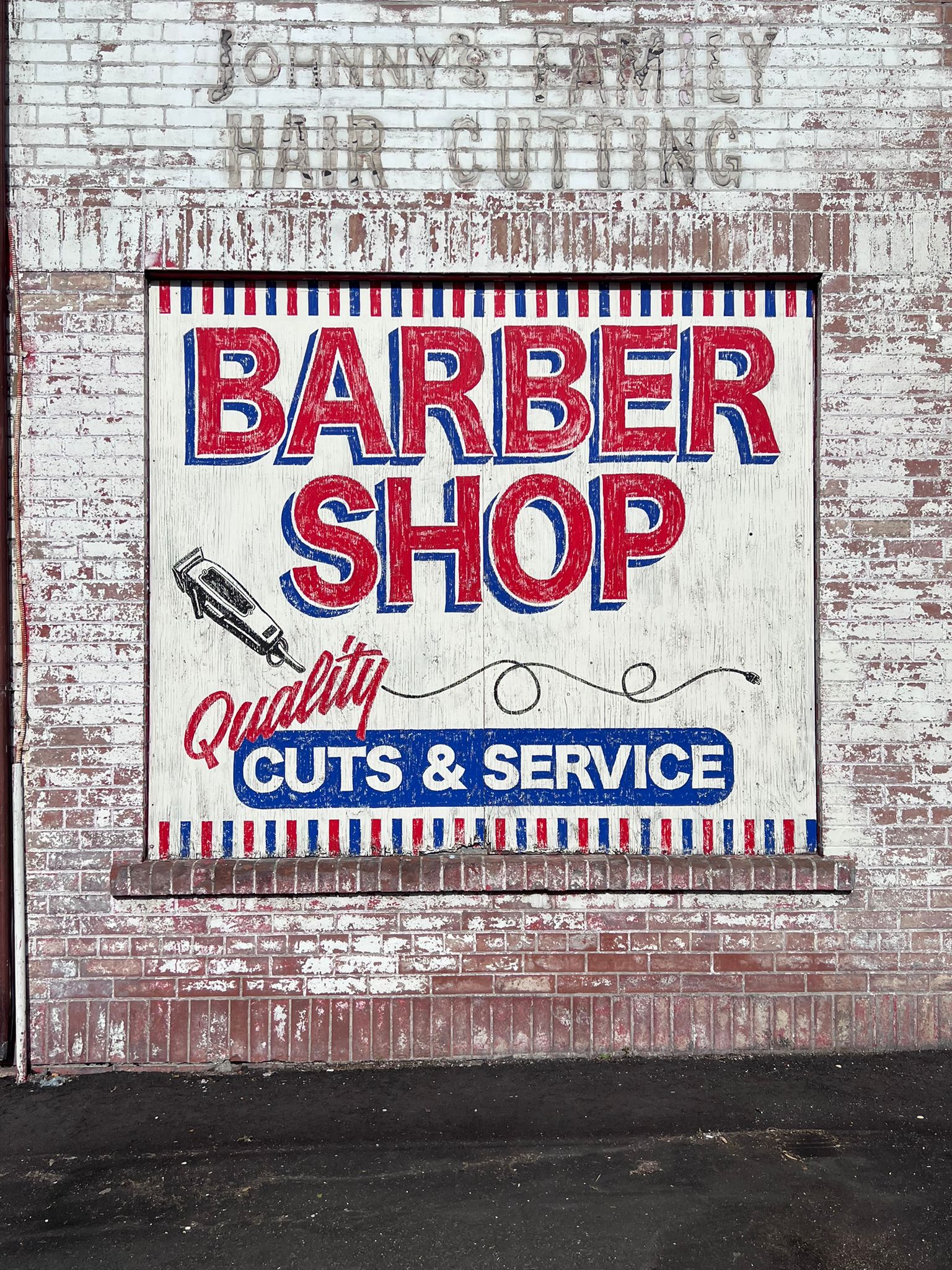 Painted mural reading "Barber Shop. Quality Cuts & Service" in red and blue type. Shadow of "Johnny's Family Hair Cutting" still visible above the freshly painted sign from the previous barber shop