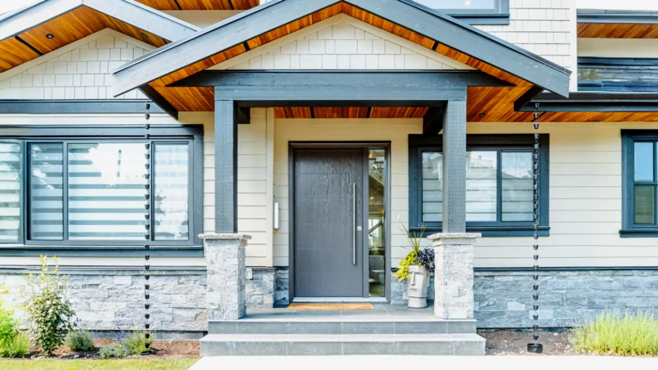 Modern gray front door entrance with glass panel and stone pillar accents in custom Burnaby home
