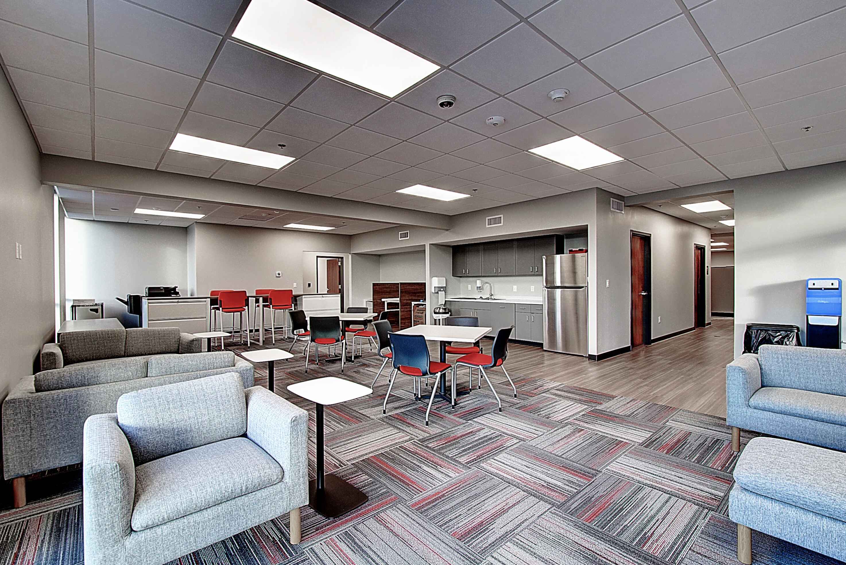 A modern office space with comfortable seating, a desk area, and neutral decor. Bright overhead lighting is visible.