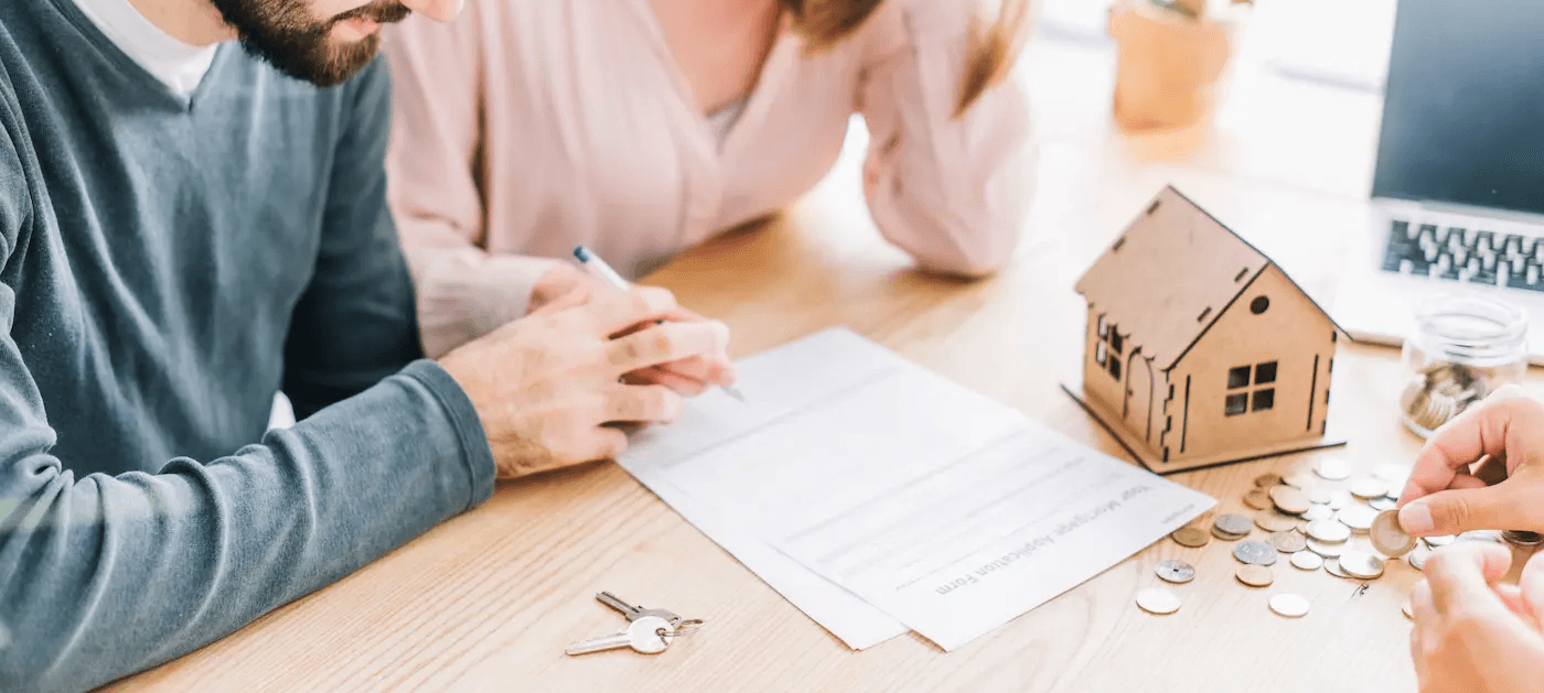 Ein Paar sitzt einem Berater gegenüber und füllt einen Vertrag aus für die Baufinanzierung für ihr Eigenheim